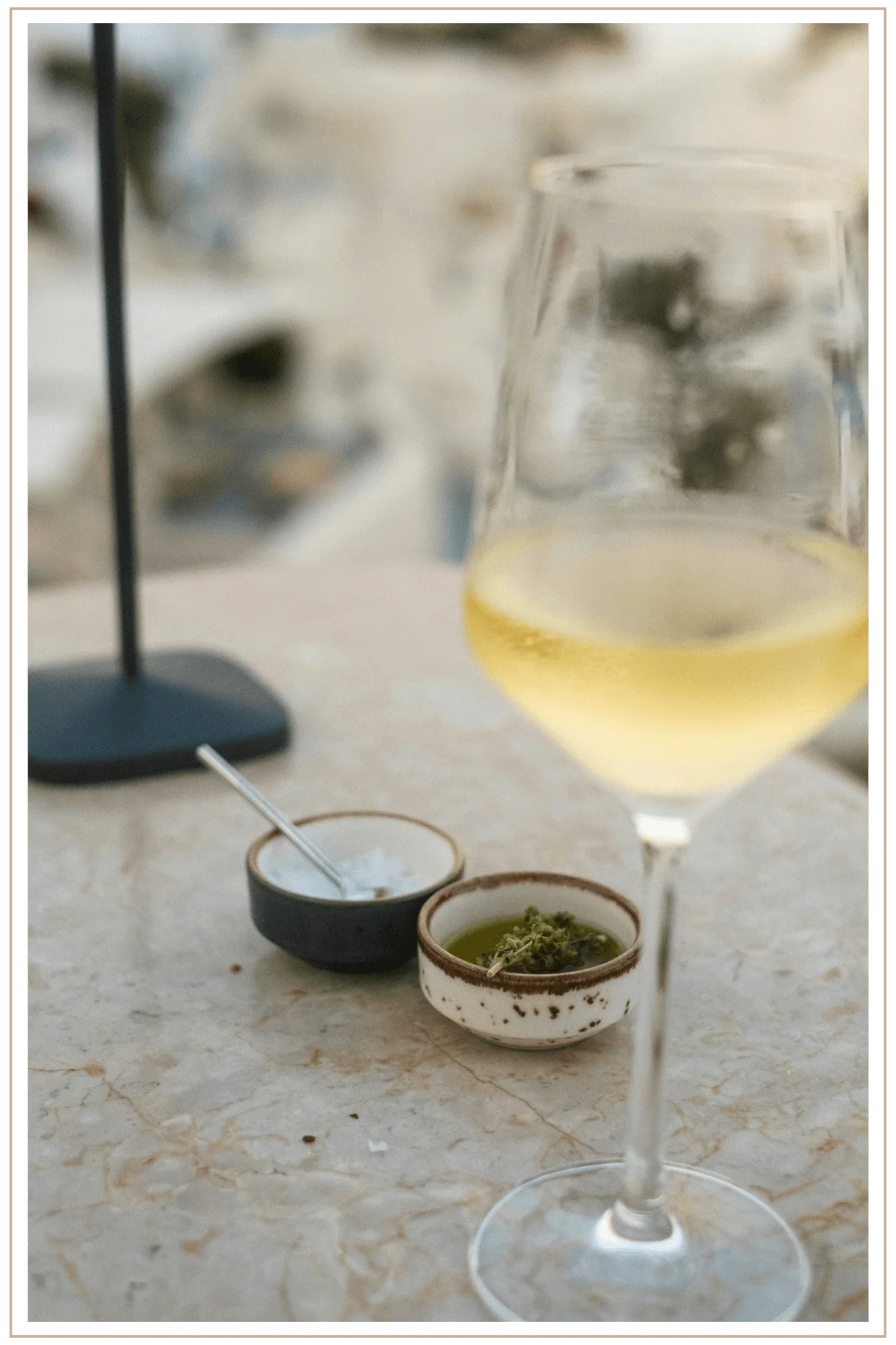 A crisp glass of Greek white wine with appetizers on a table overlooking the architecture of Santorini, Greece, part of a vetted multi-city European trip.