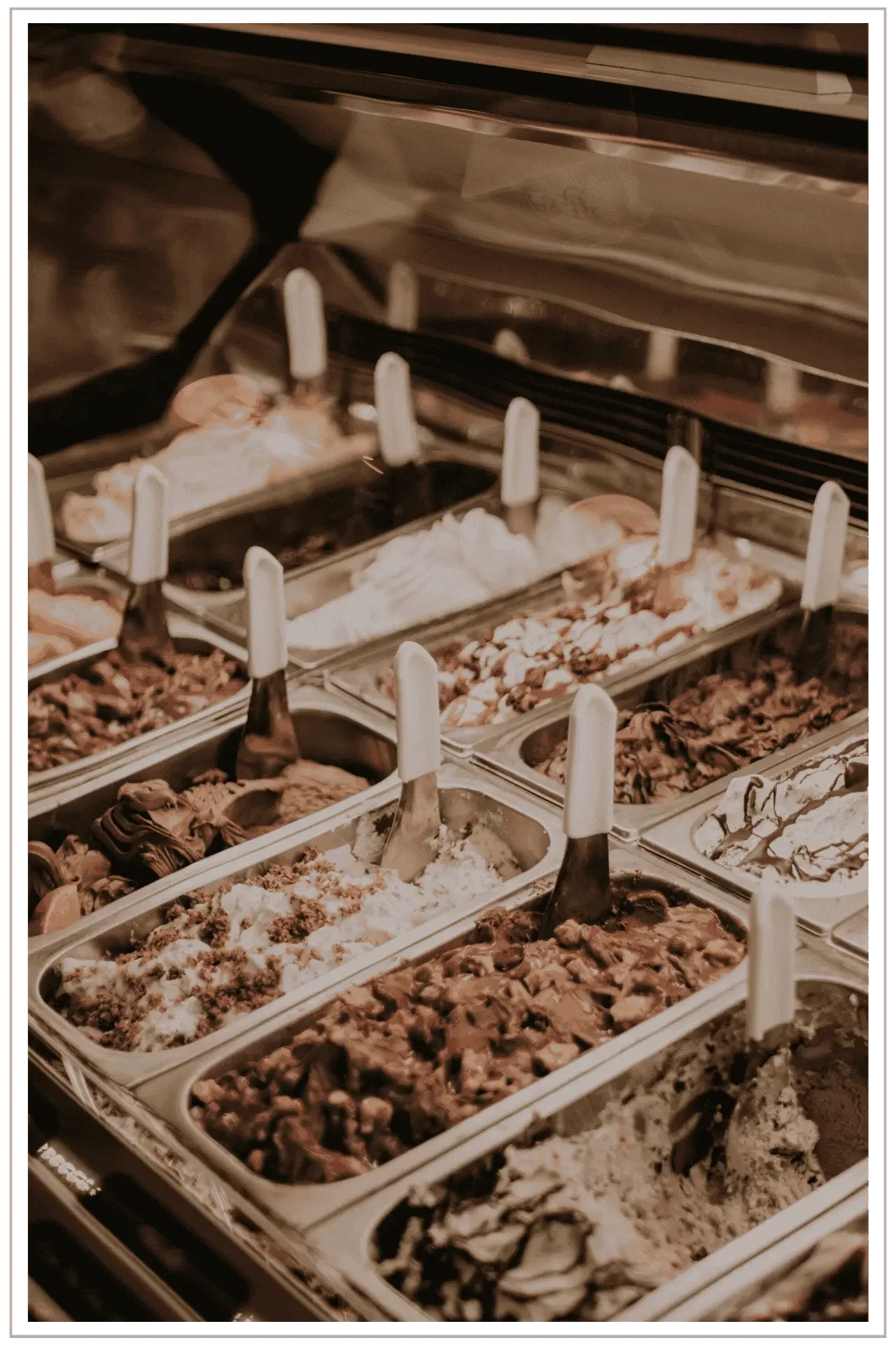 Close-up editorial shot of waves of artisan Italian gelato in a display case, featuring warm cream and chocolate tones in soft, golden lighting.