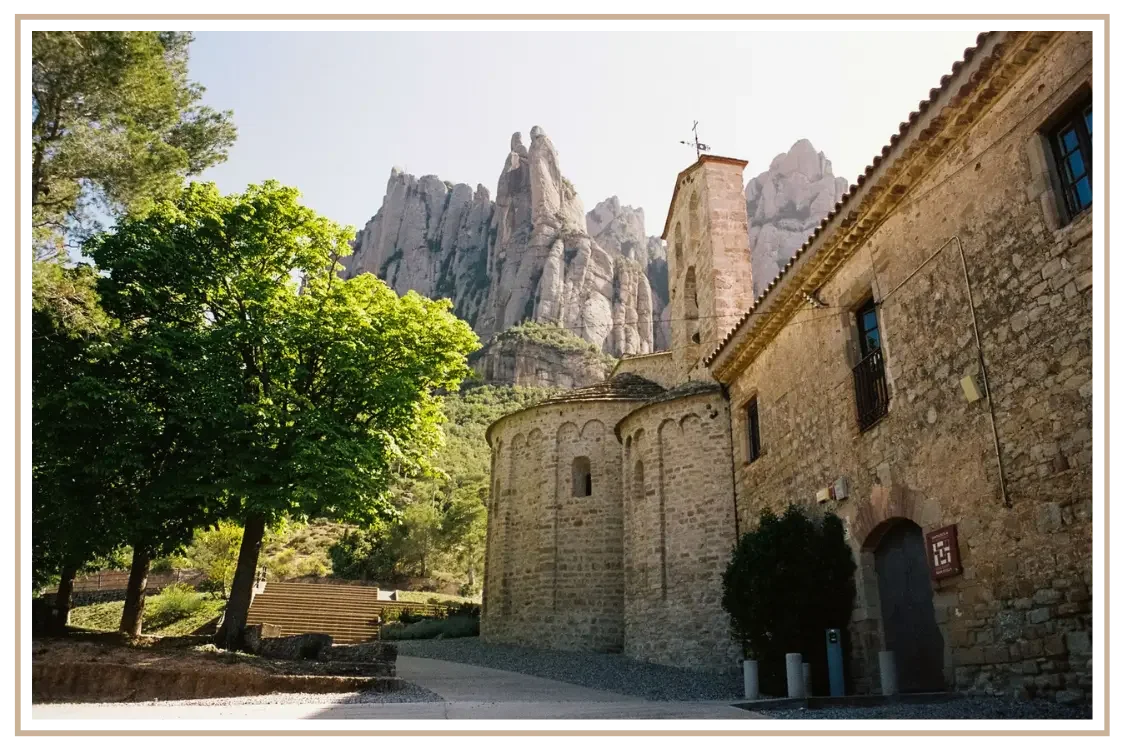 The historic Romanesque church of Santa Cecília de Montserrat framed by the dramatic jagged rock peaks of Montserrat mountain makes a perfect day trip from Barcelona, Spain. Custom Spain itinerary design for US travelers by US-based travel advisor De