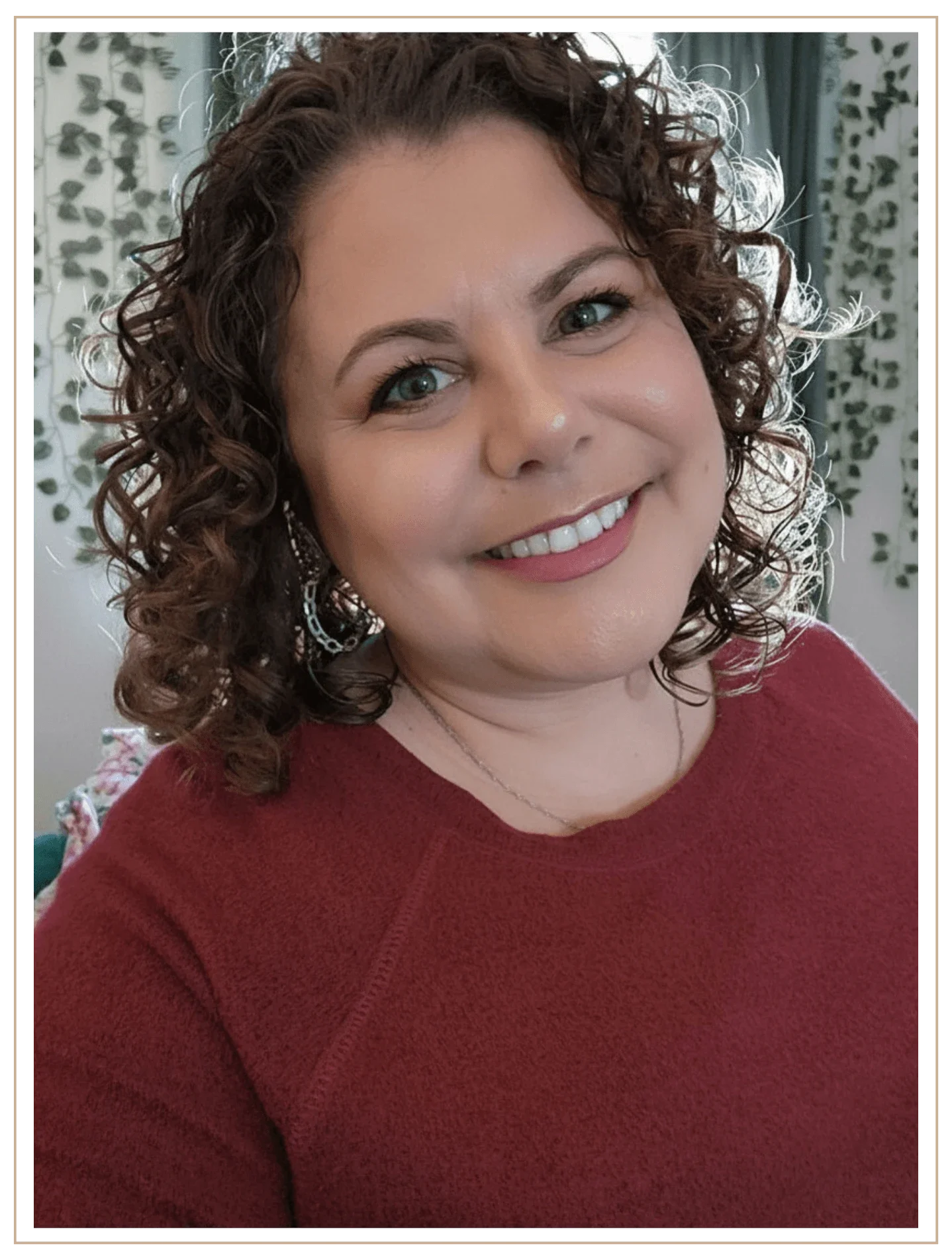 A photo of Denise Kubica, Luxury Travel Advisor and Owner of Mindset Travel, wearing a terracotta sweater, smiling at the camera, with ivy in the background.