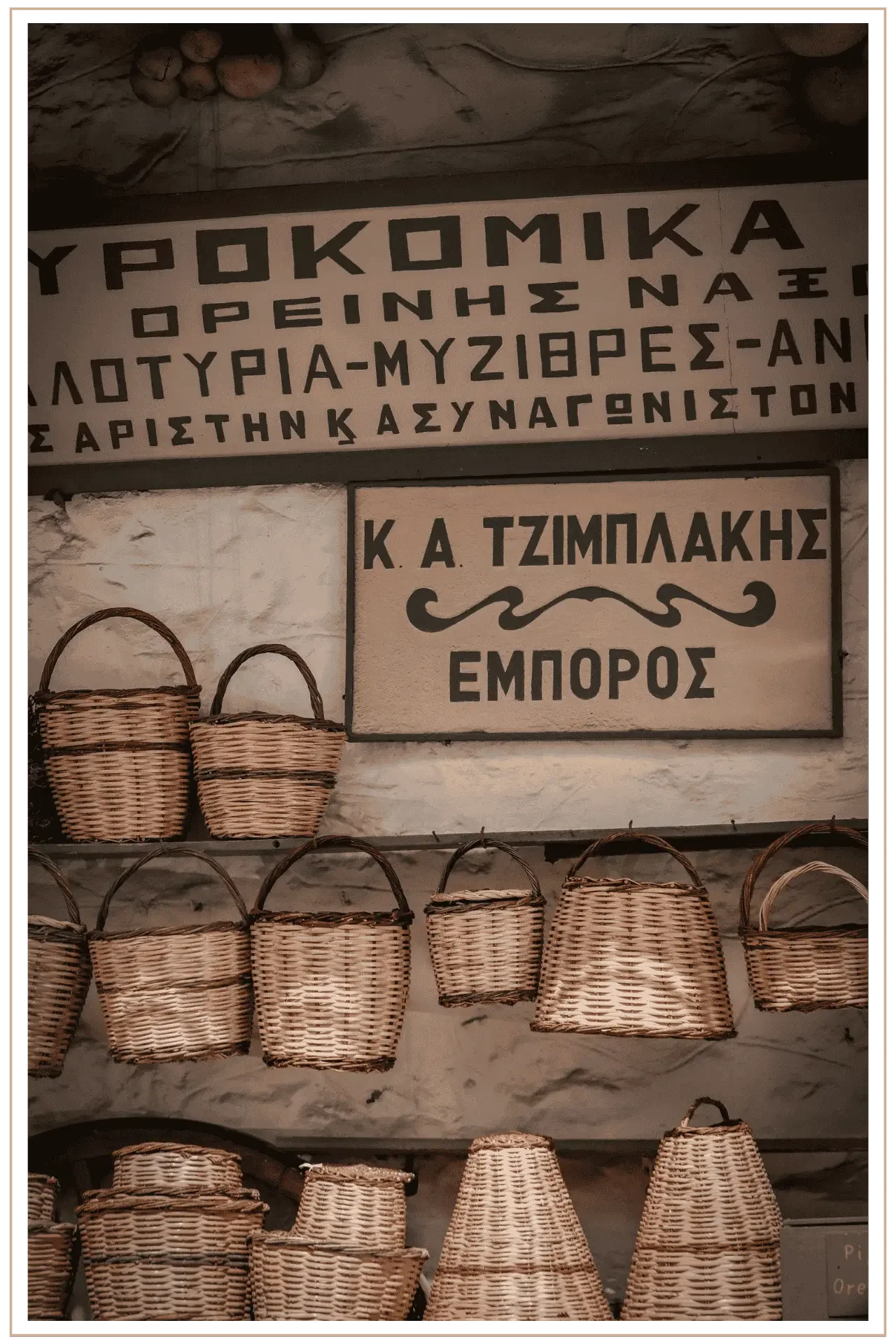 A local shop on Naxos in Greece with a display of wicker baskets for sale. Some are hanging on the wall while others are on shelves, and there are signs in Greek hanging on the wall above them.