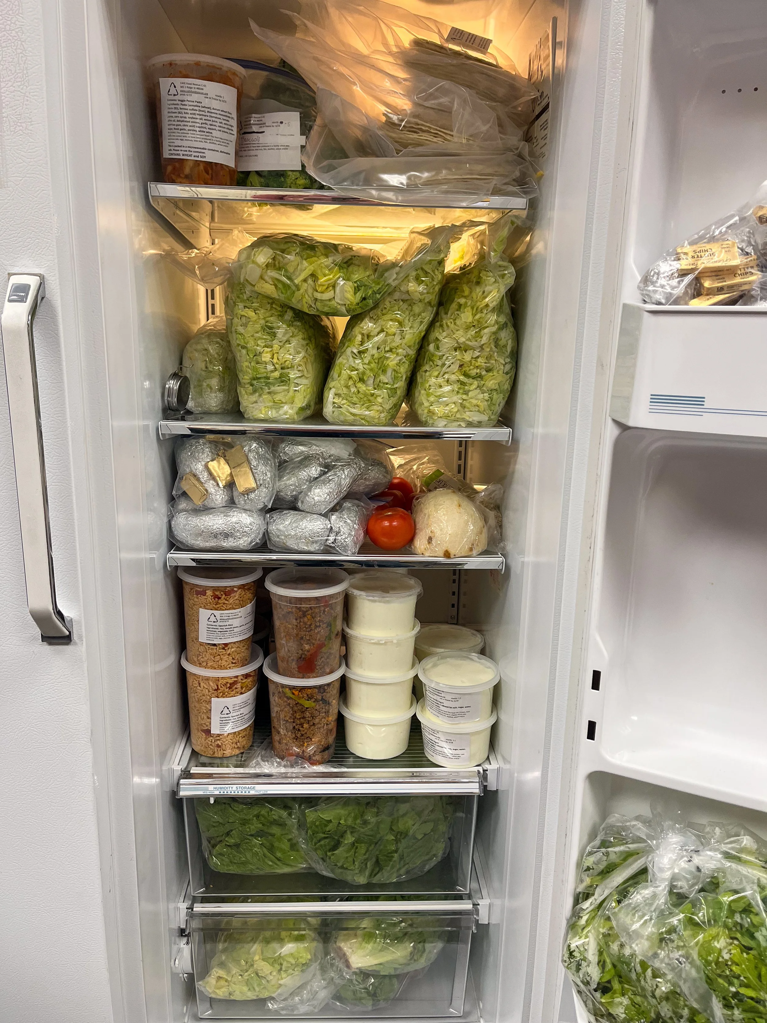 CAFE Food Rescue access point fridge stocked with rescued greens, vegetables, and prepared meals