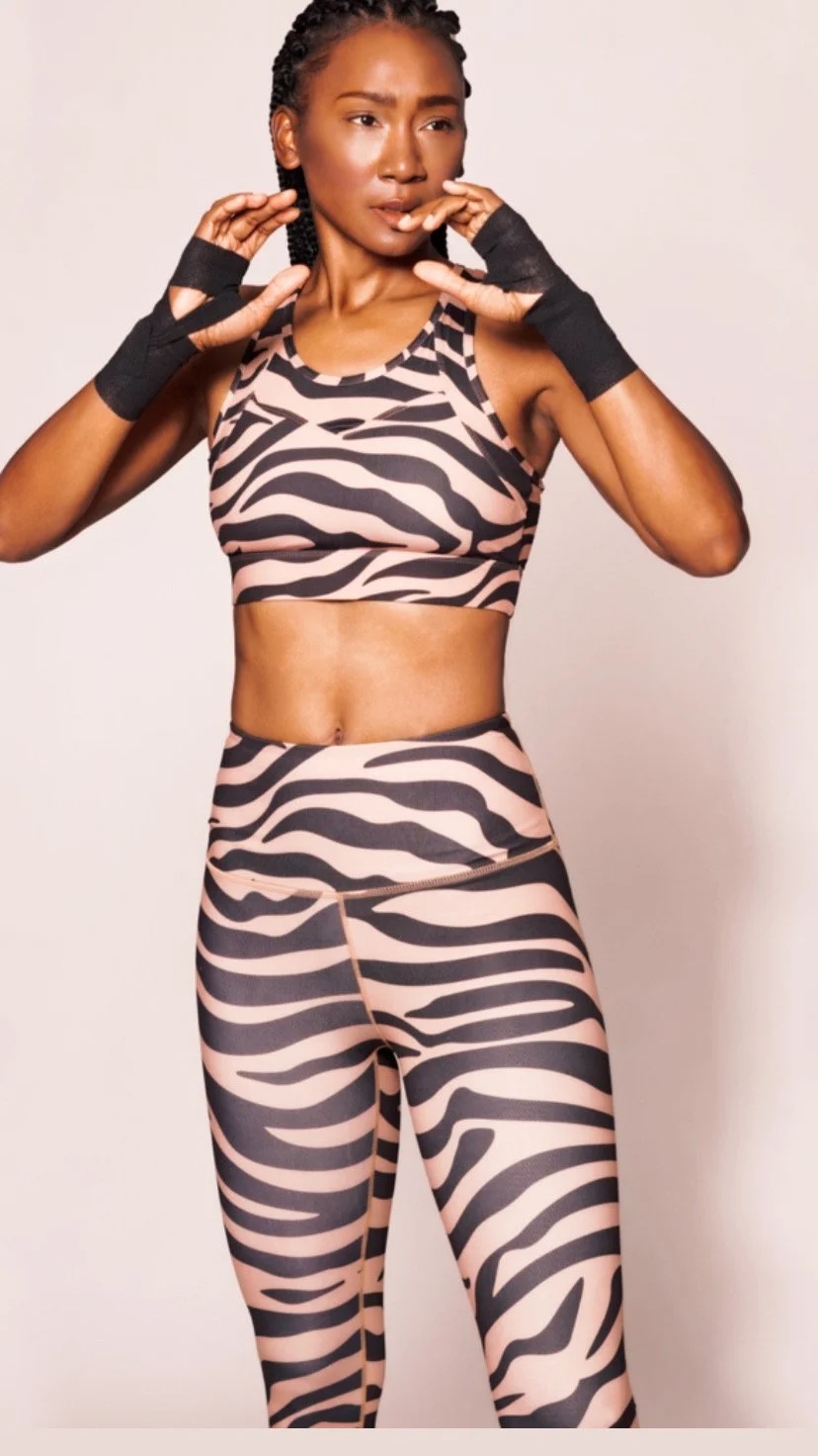 A fitness woman in a zebra print sports bra and leggings poses with yoga gloves, looking to the side with a thoughtful expression.