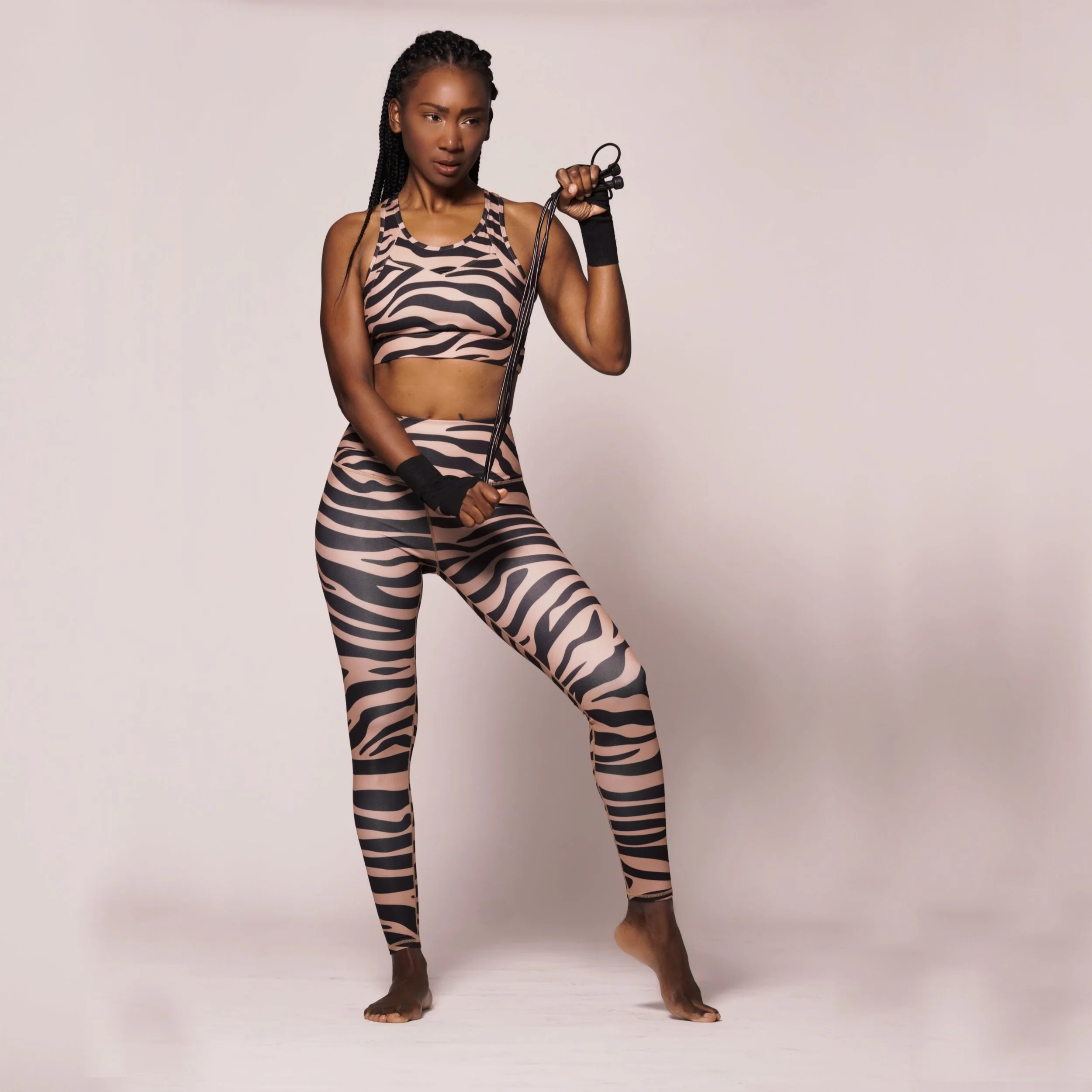 Woman dressed in zebra print athletic wear holding a jump rope, standing on a white floor against a plain light background.