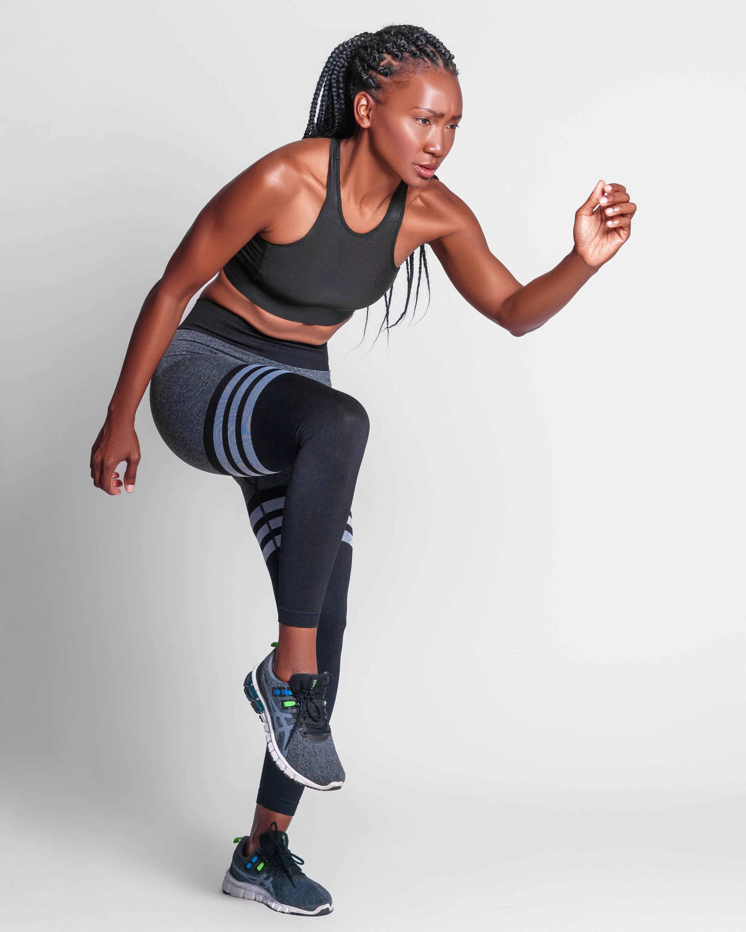 A woman in athletic clothing is running in place against a plain grey background.