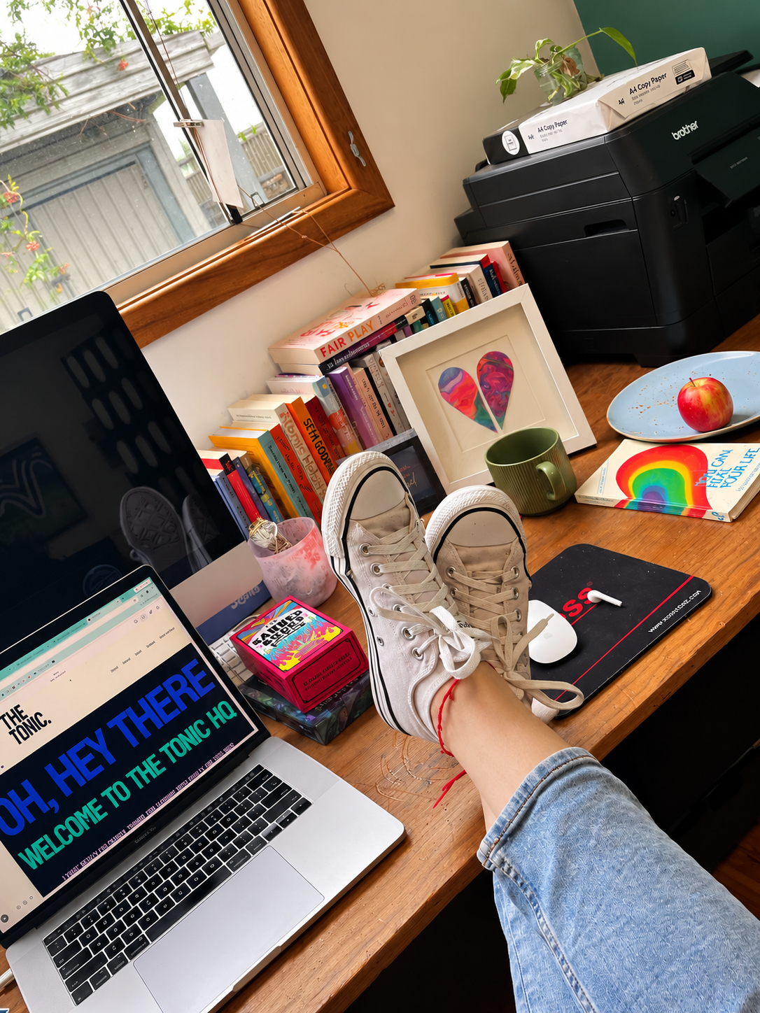 Creative business owner working from home with Converse sneakers on, feet up at a colourful home office desk.