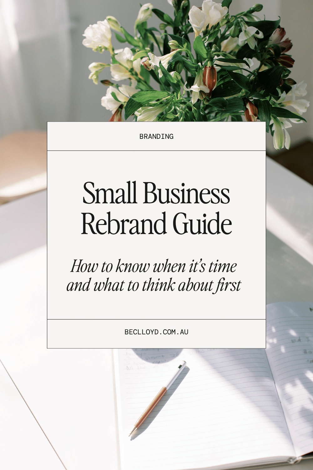 'Small Business Rebrand Guide' text overlay in a white box set on an image of a desk with an open notebook and a pen, a vase with white flowers in the background.