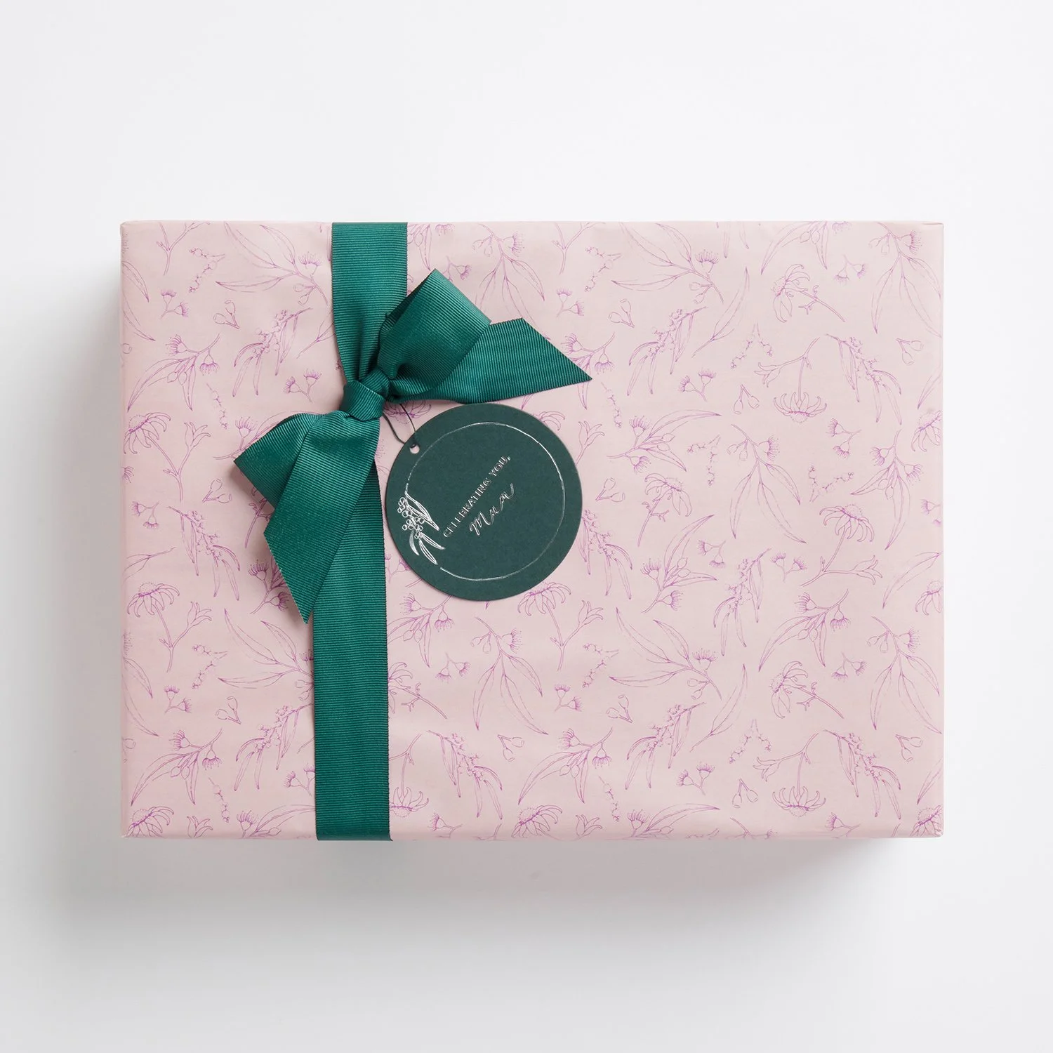 A wrapped gift box with pink floral paper, a green satin ribbon tied in a bow, and a round green gift tag.