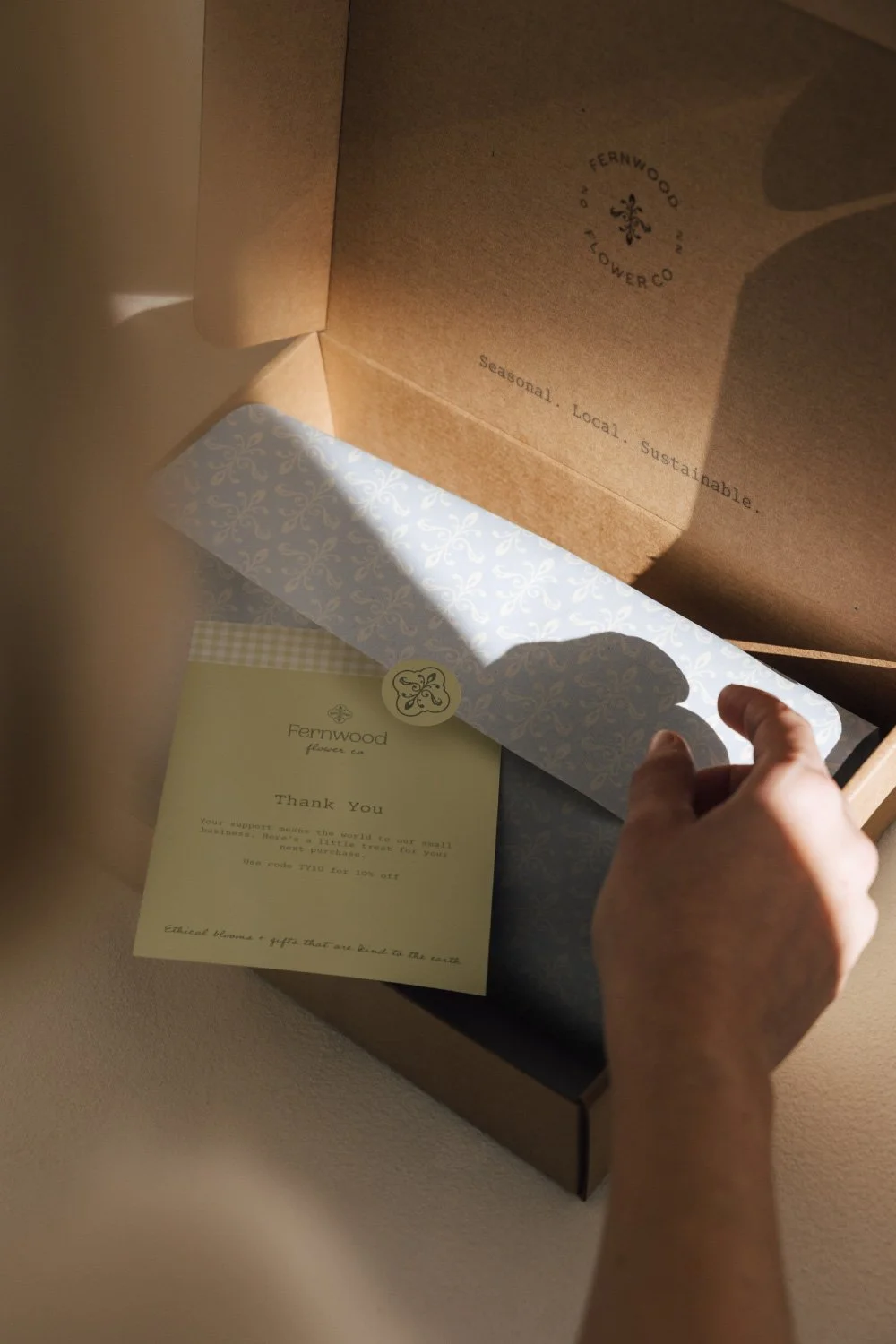 Open cardboard box with Fernwood Flower Co. branding, containing a thank you note and decorative tissue paper.