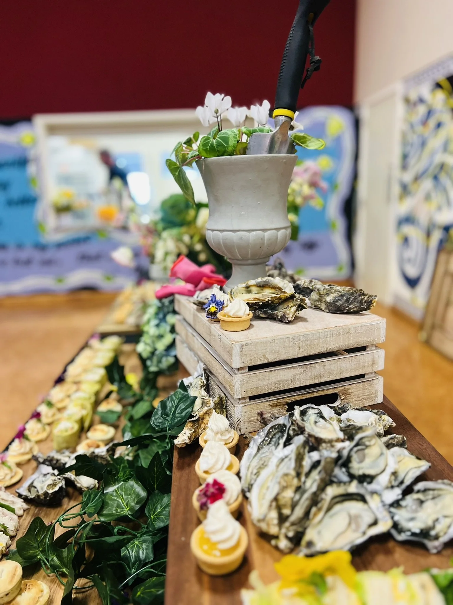 Display of seafood and appetizers on a table with a floral centerpiece, mussels, oysters, cupcakes, and greenery in the background.