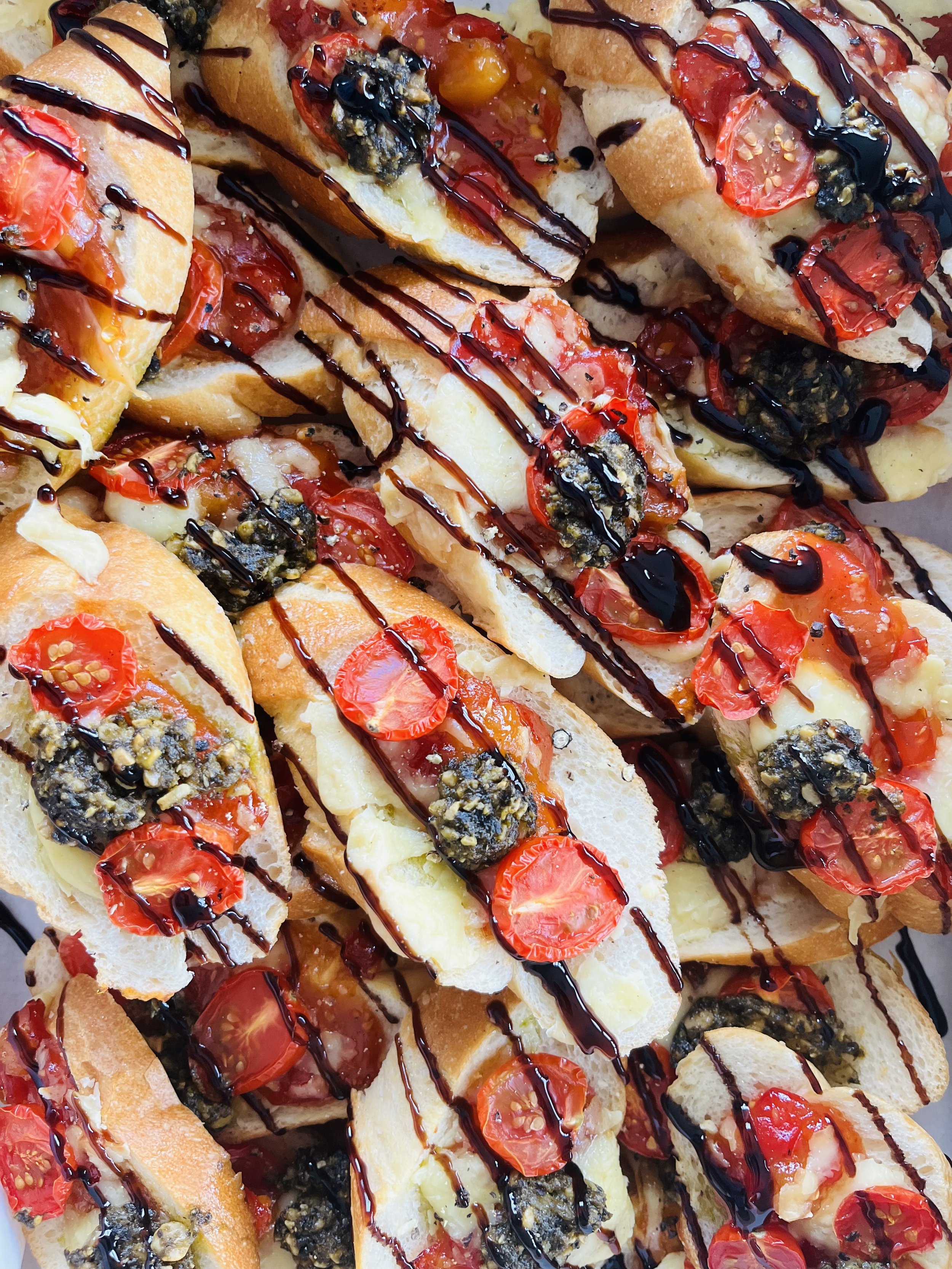 Slices of baguette topped with cherry tomatoes, black olives, melted cheese, drizzled with balsamic glaze and olive oil.