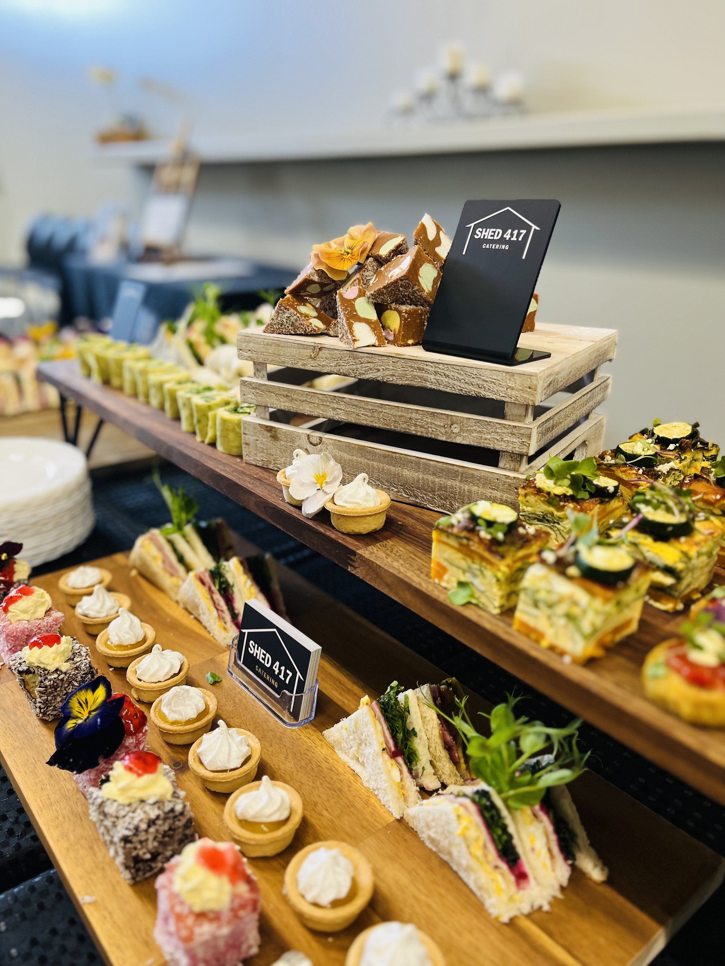 Assorted desserts including cake slices, small tarts, and pastries displayed on wooden and rustic trays at a catering event.