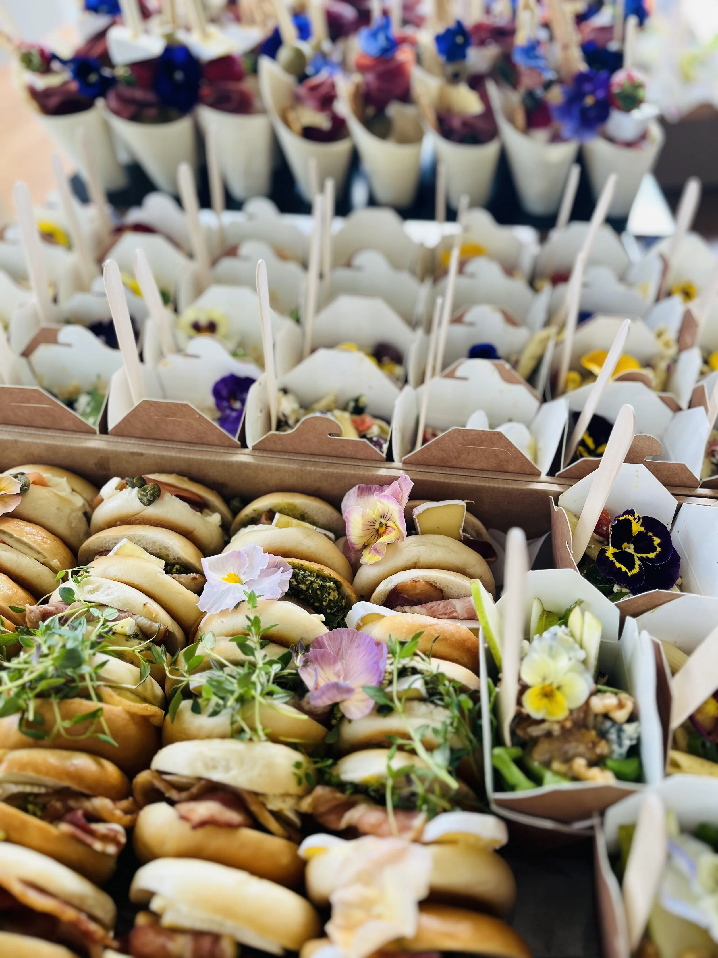 Assorted small sandwiches and appetizers decorated with edible flowers on a table.