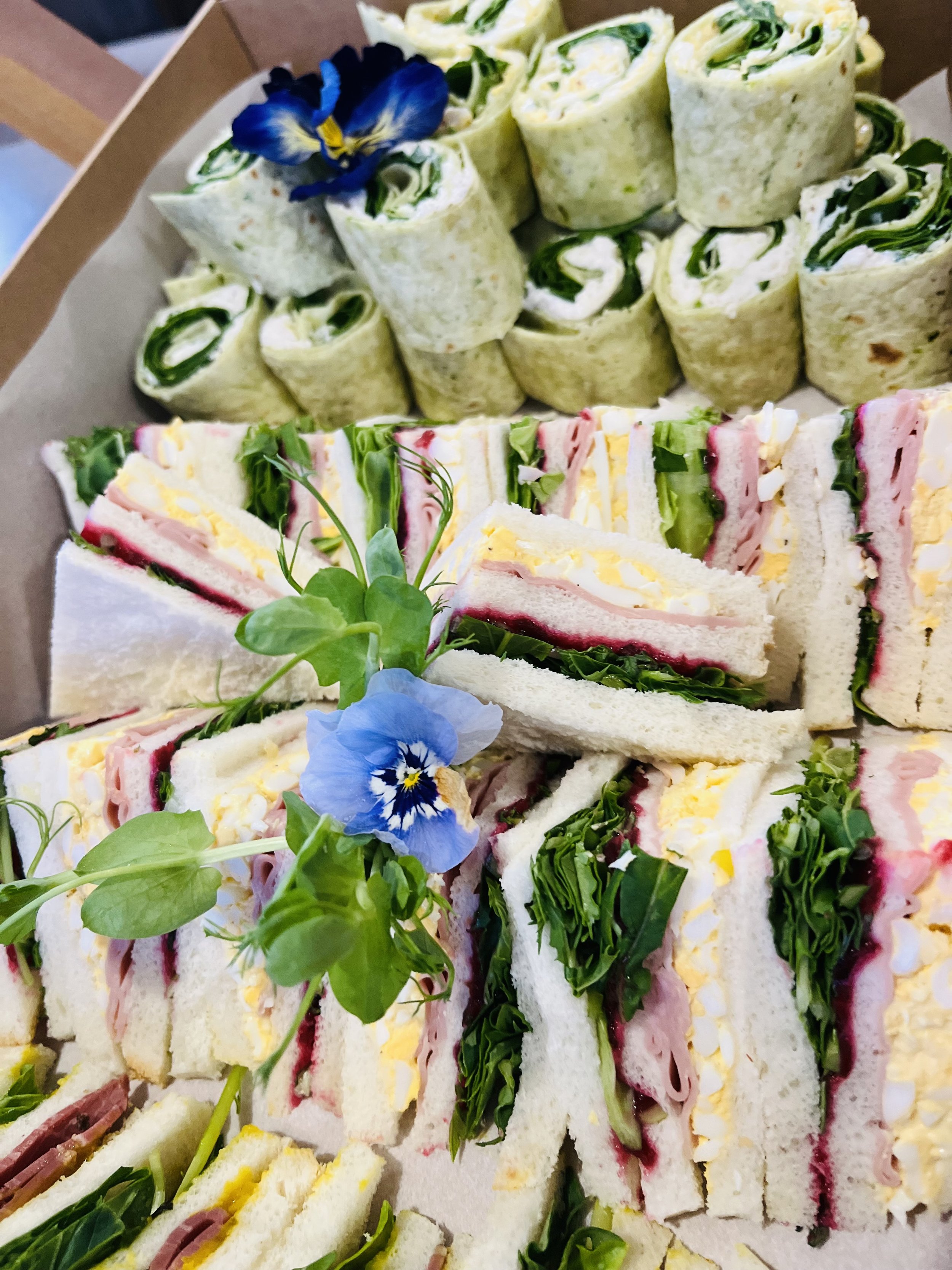 Tray of pinwheel sandwiches with green herbs and a blue edible flower.
