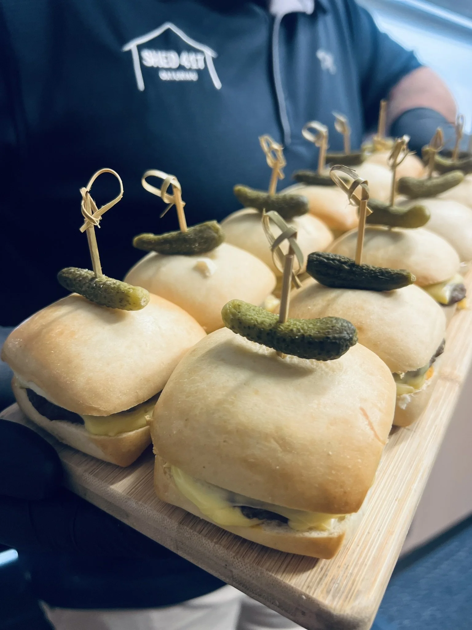 Tray of small sandwiches with bread rolls, cheese, and pickles, each secured with a toothpick.