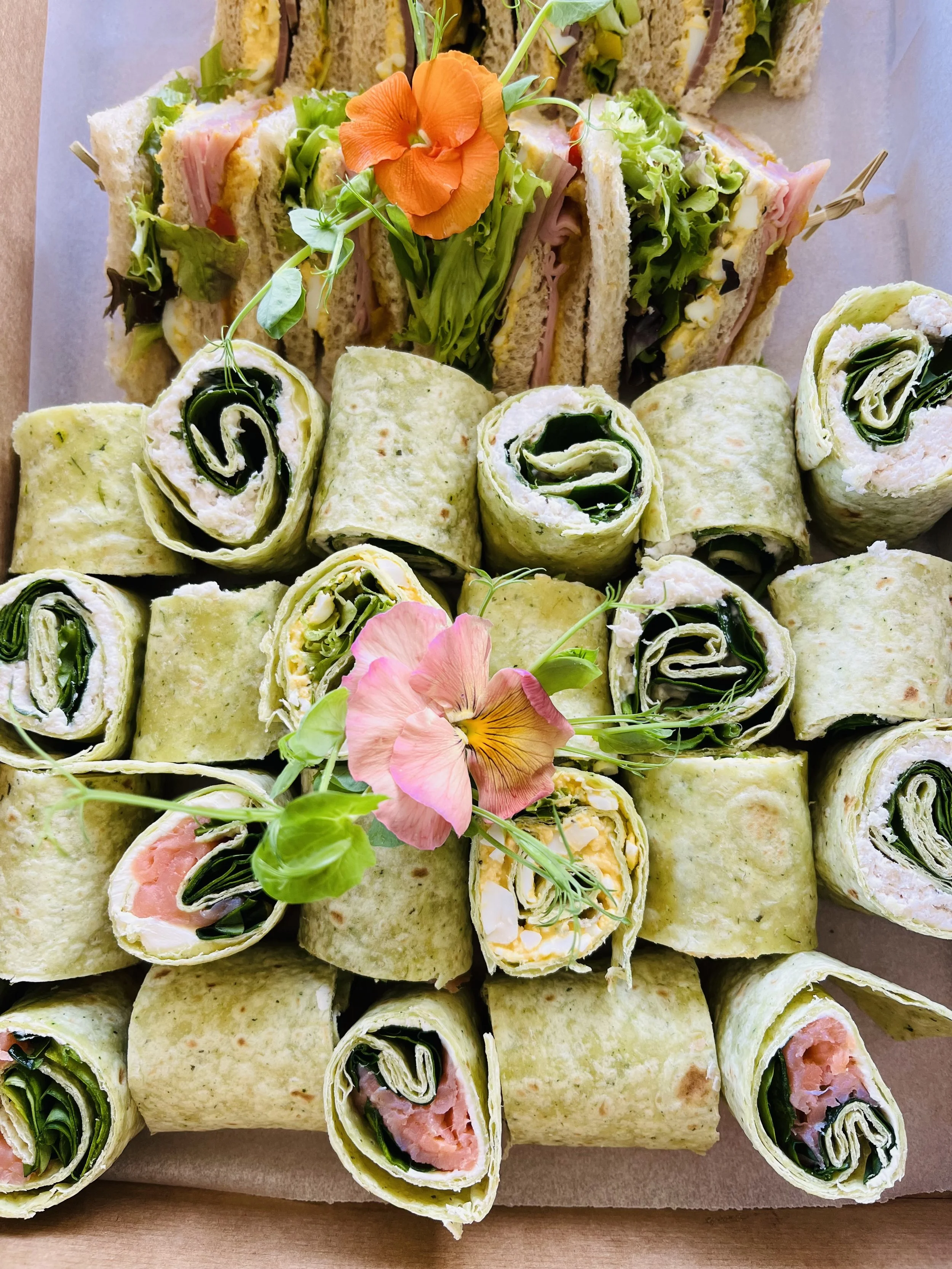 Assorted sandwiches and wraps decorated with edible flowers.