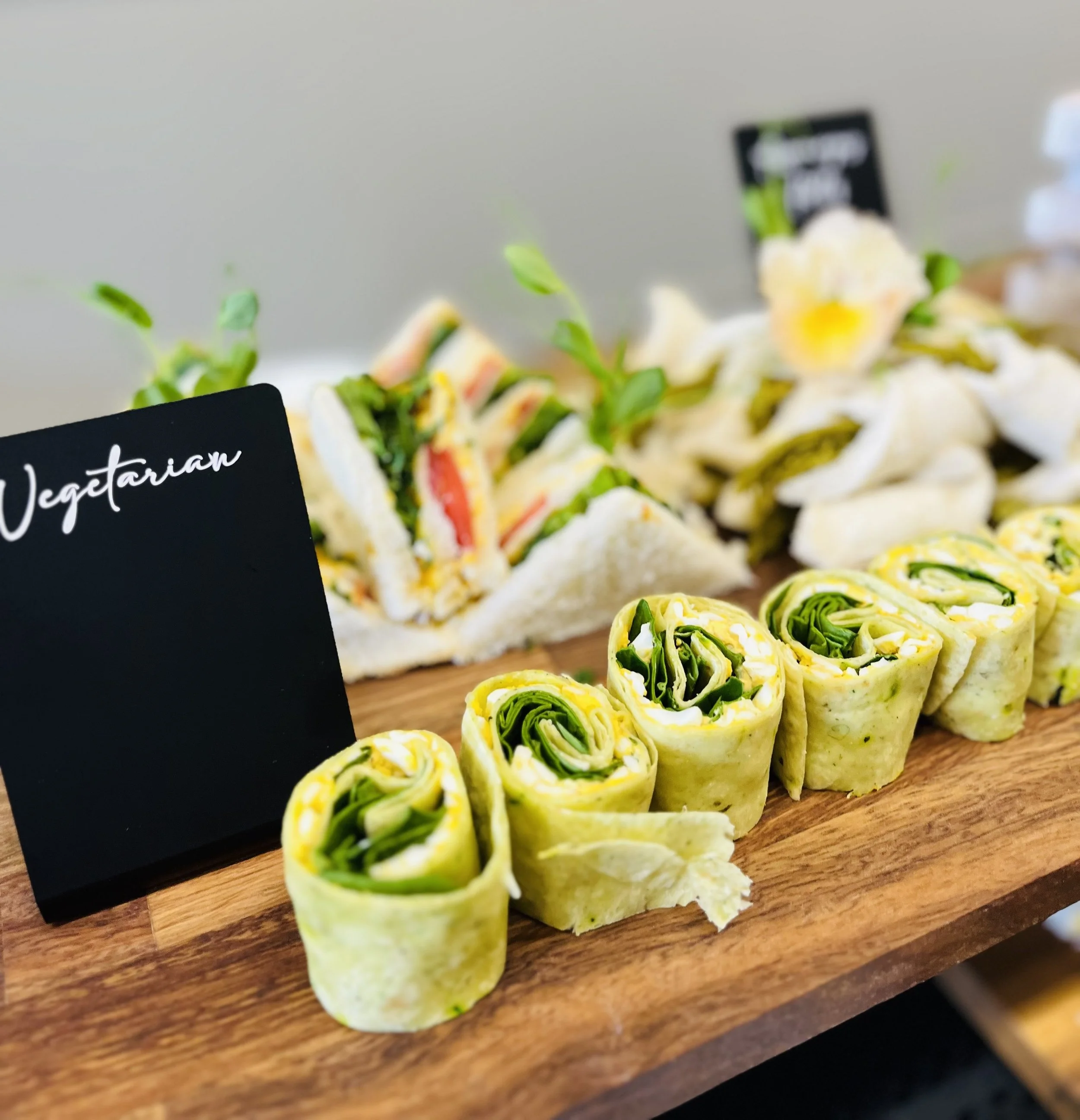 Vegetarian pinwheel wraps with green leafy vegetables, cheese, and mustard on a wooden board with a black 'Vegetarian' sign.