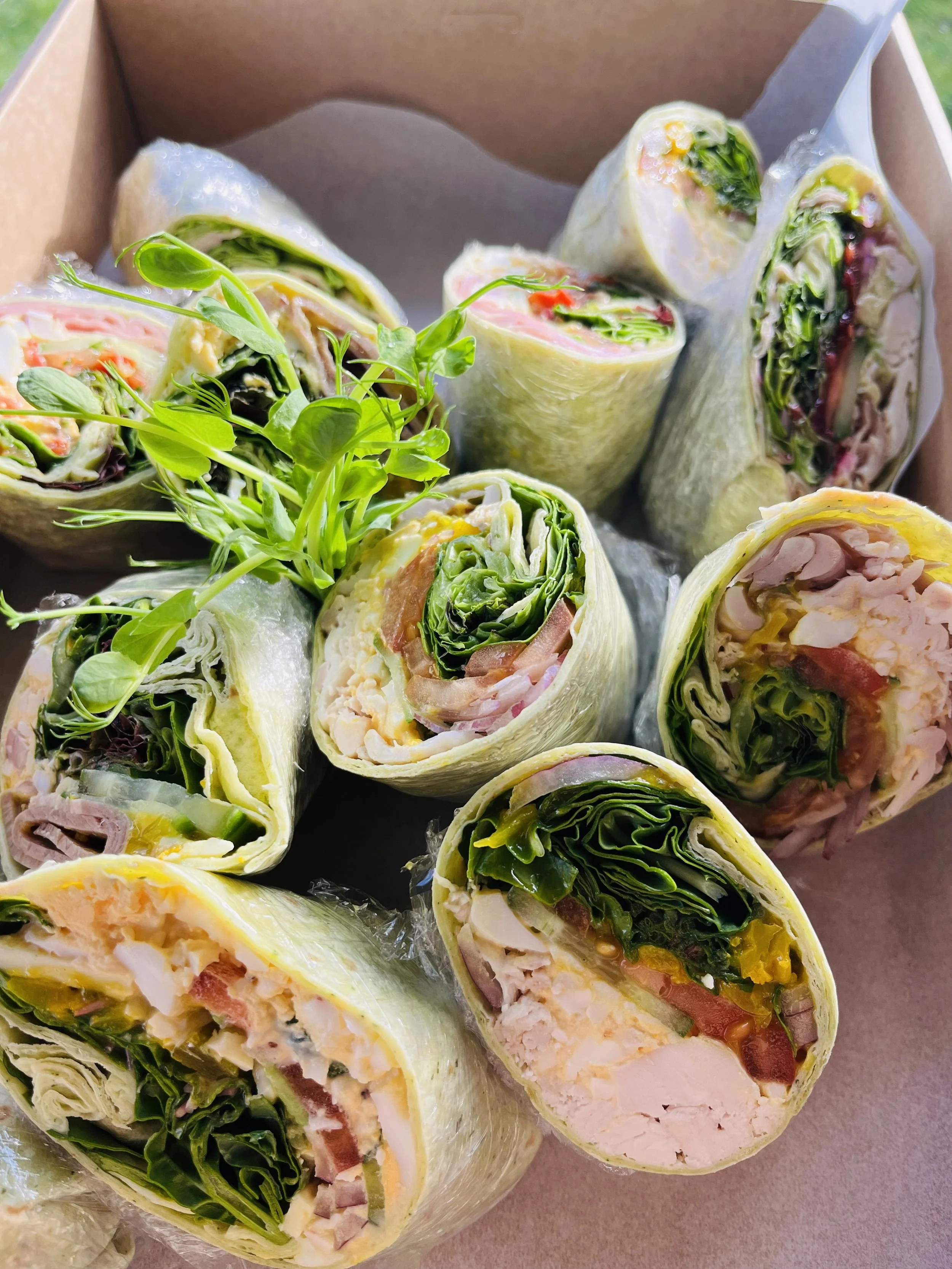 Assorted fresh vegetable and chicken spring rolls in a brown cardboard box with a small bunch of microgreens.