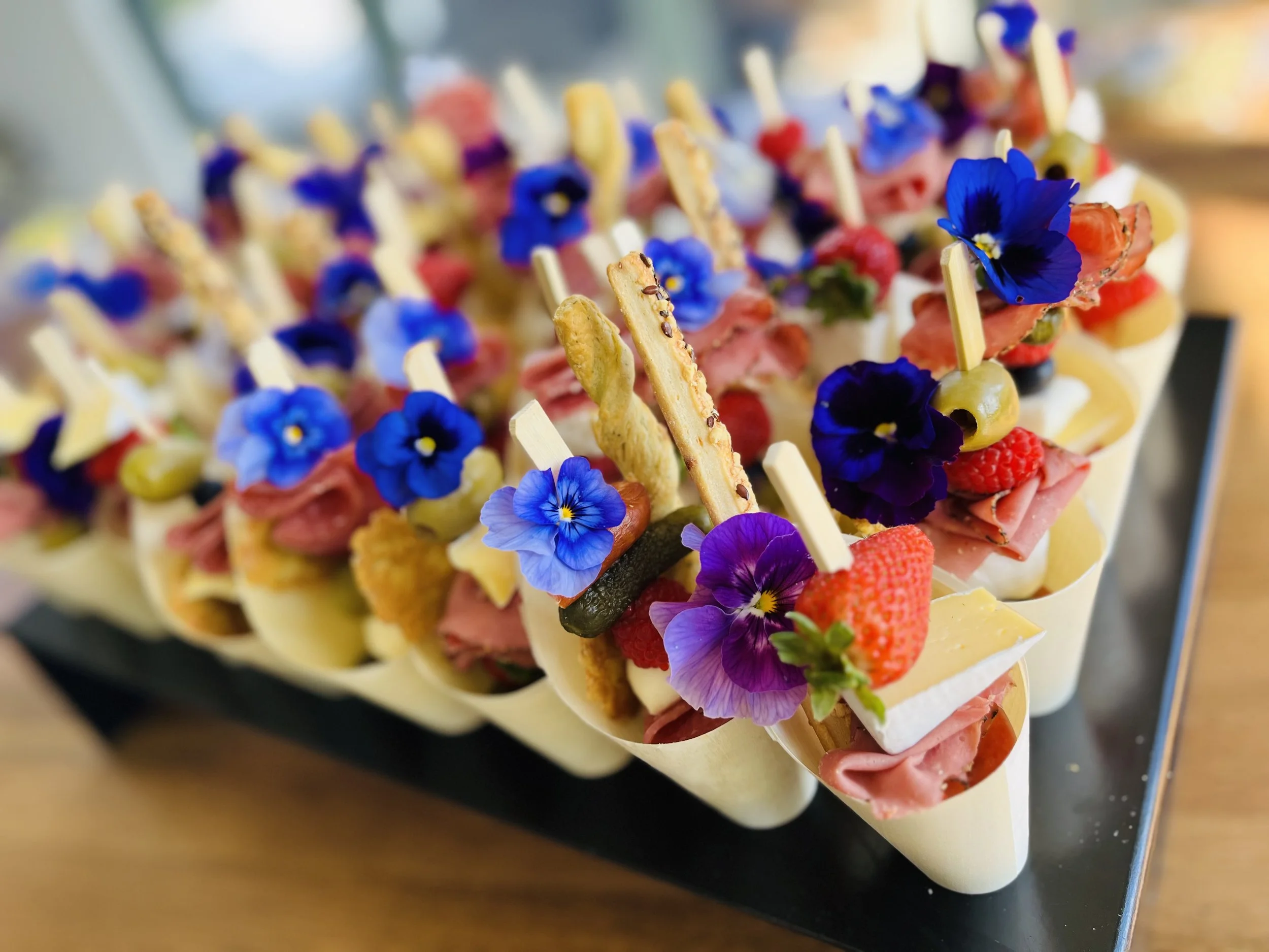 A tray of decorative appetizers with edible flowers, berries, cheeses, meats, and crackers.