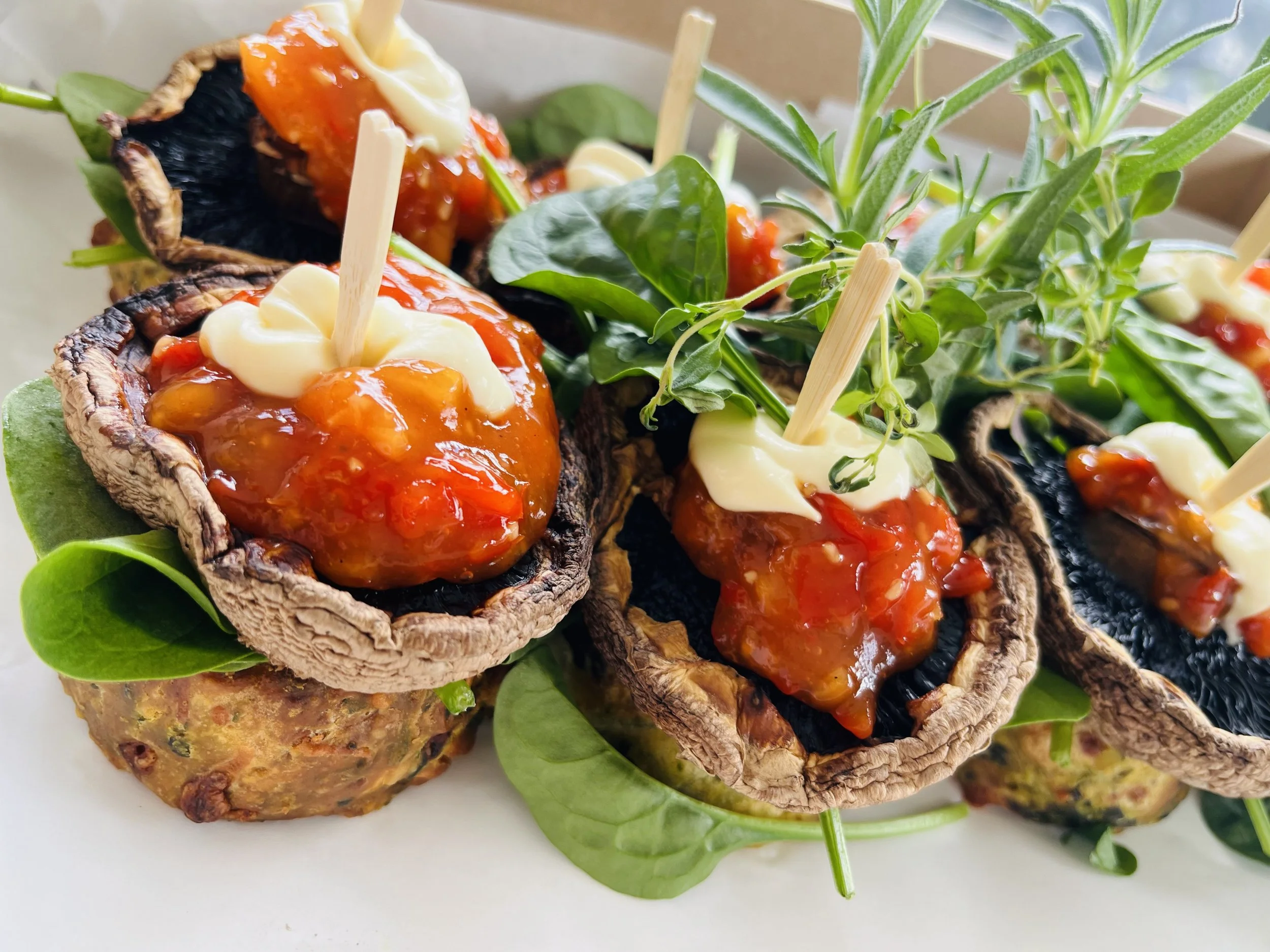 Stuffed mushroom caps topped with cheese and tomato sauce, garnished with fresh greens.
