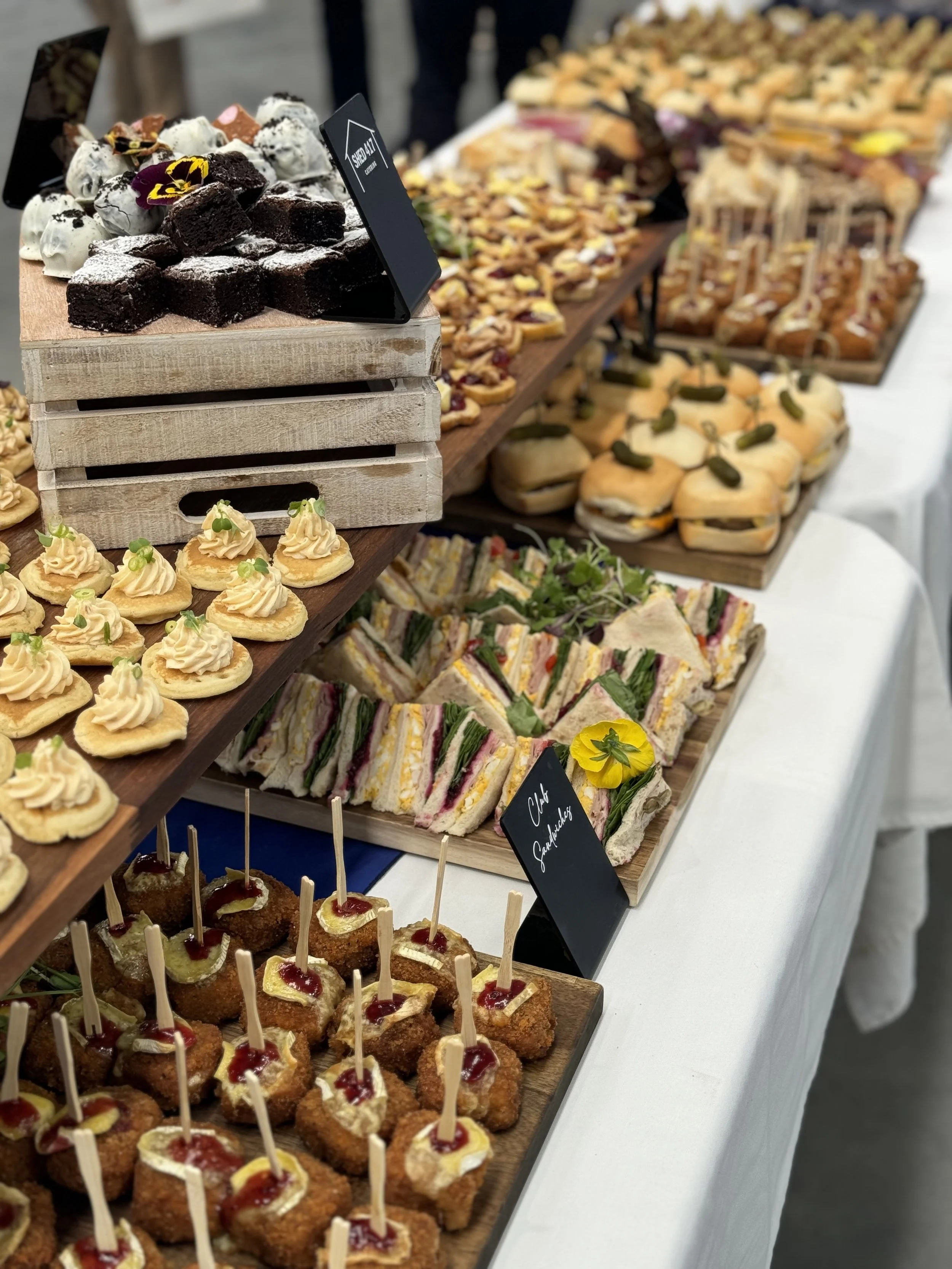 Assorted finger foods and desserts on a white table, including small sandwiches, mini cakes, and appetizers.