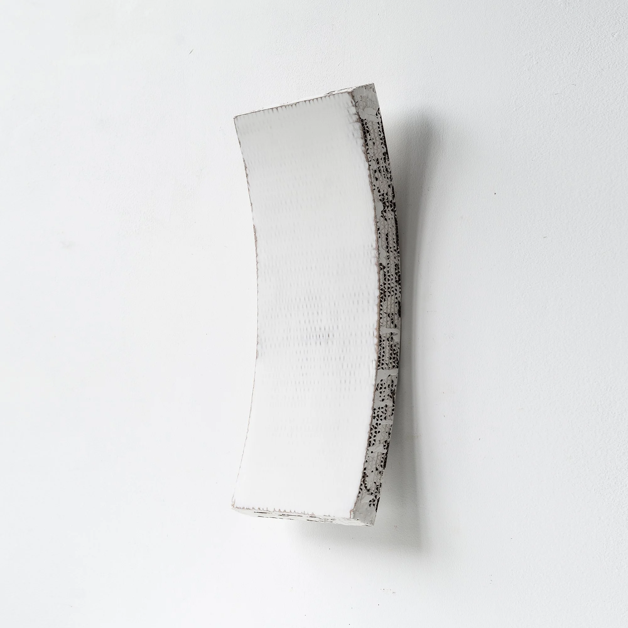 Curved white ceramic sculpture with textured edges on a white background.
