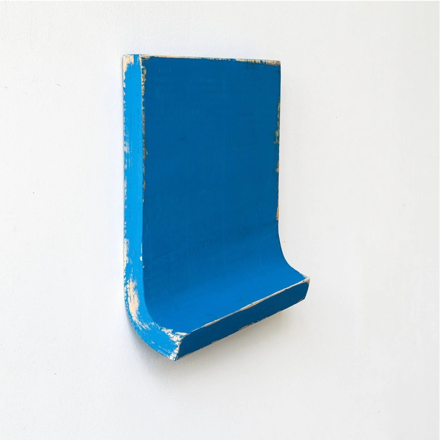 A blue, worn-out wooden shelf mounted on a white wall, with a curved bottom edge.