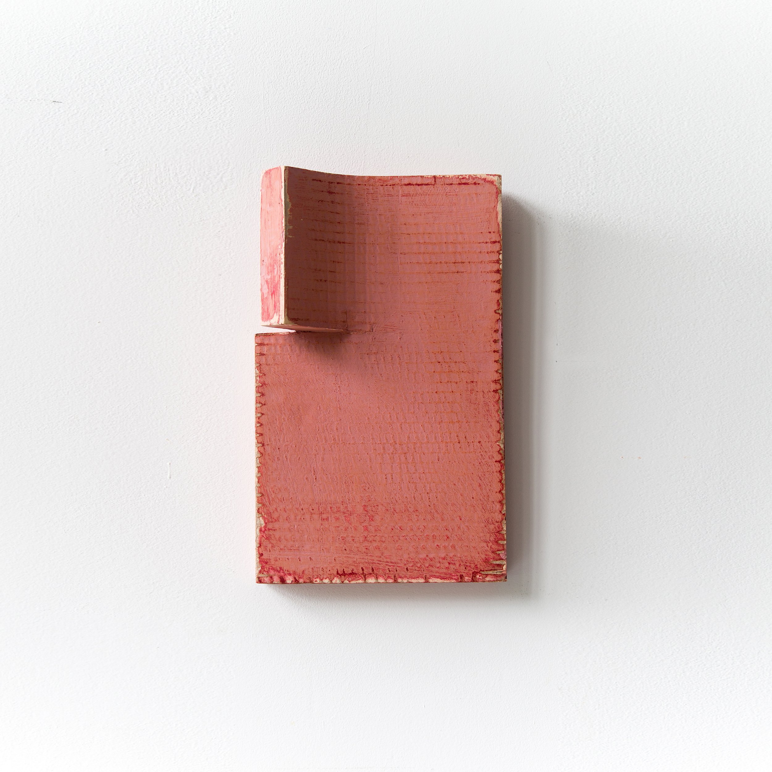 A textured rectangular pink sculpture mounted on a white wall.