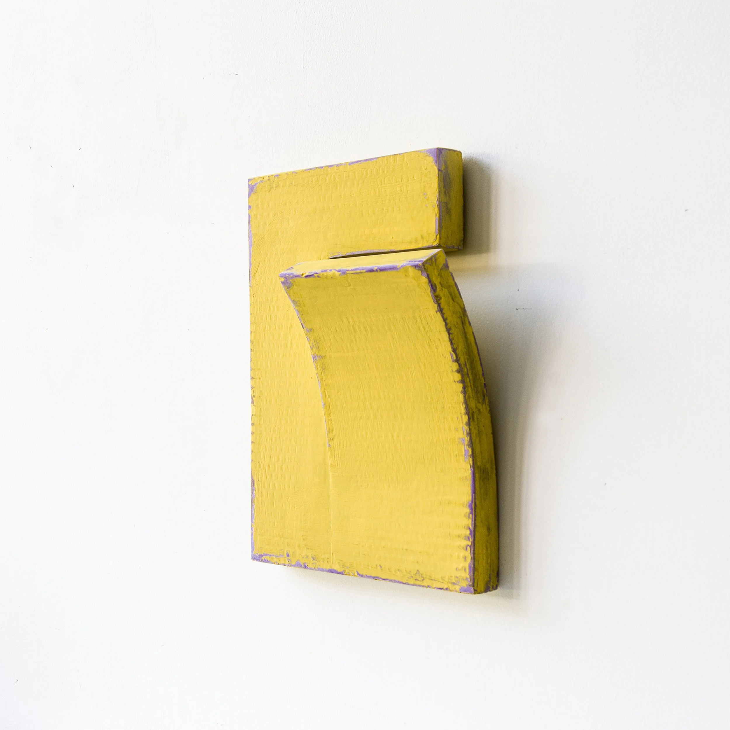 Yellow abstract sculpture with a curved shape mounted on a white wall, featuring purple edges.