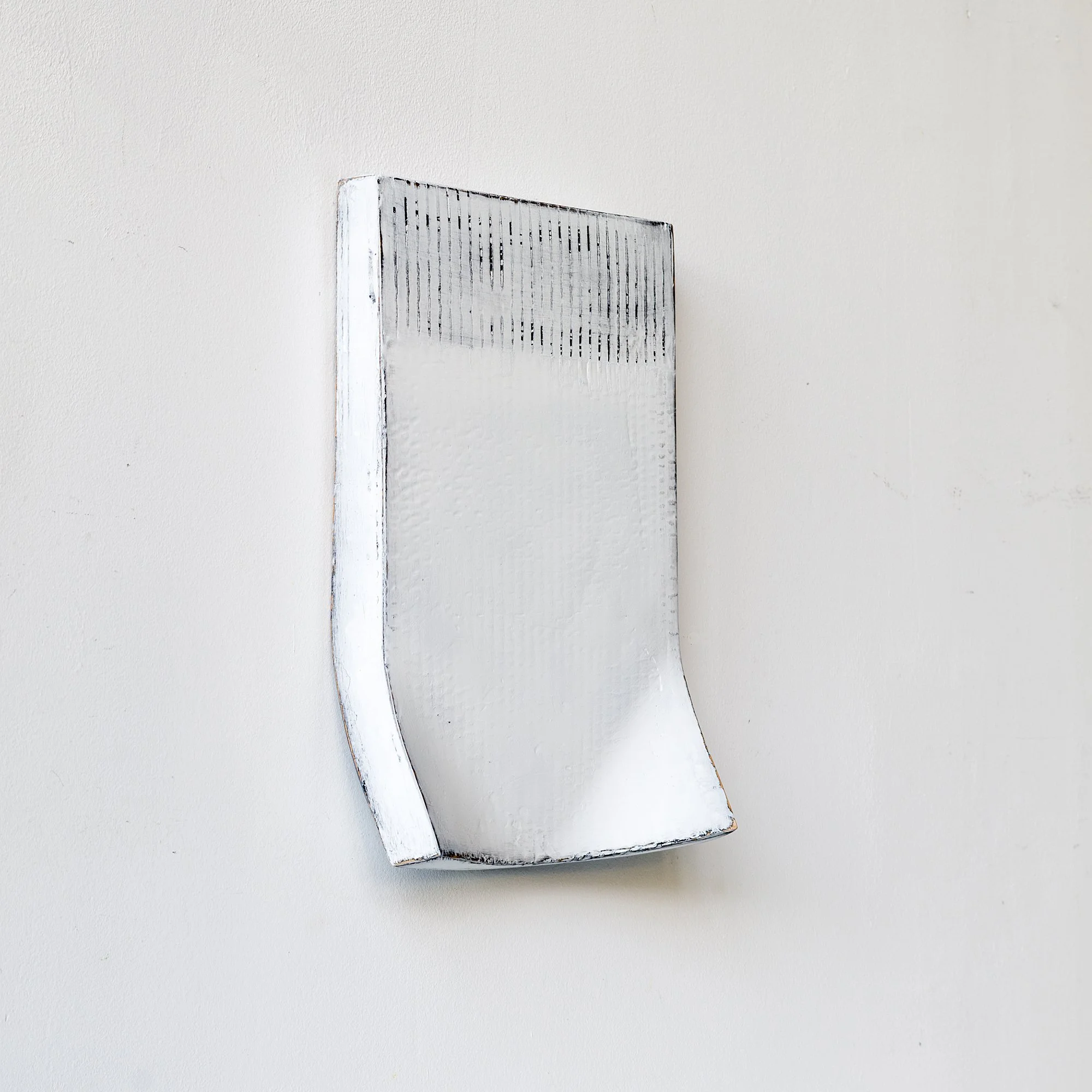 White minimalist abstract wall sculpture with texture and black edges, placed against a white background.