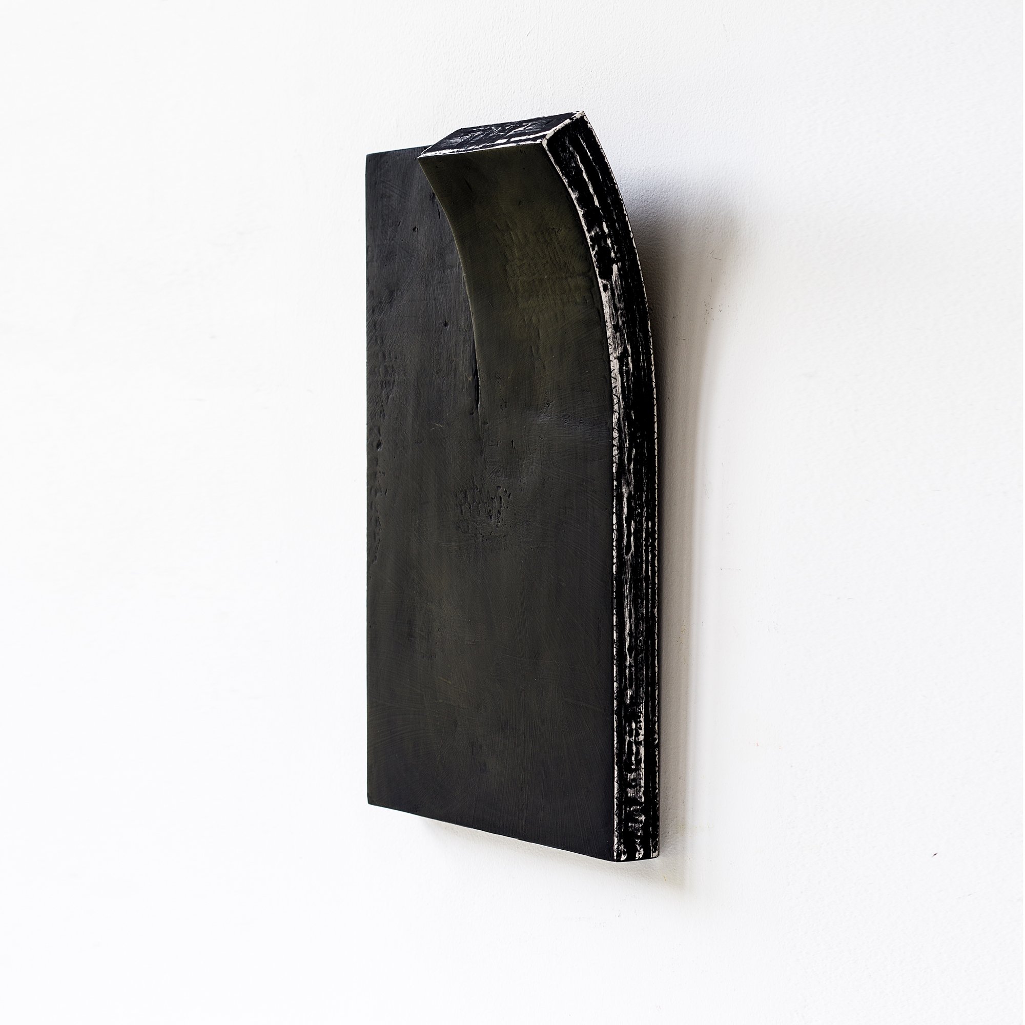 A minimalist black sculpture with a curved top edge on a white wall.