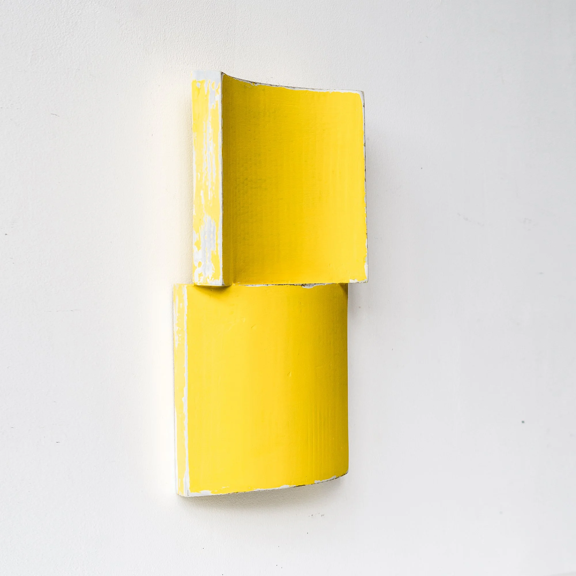 Abstract yellow wall sculpture with curved and rectangular shapes on a white background.