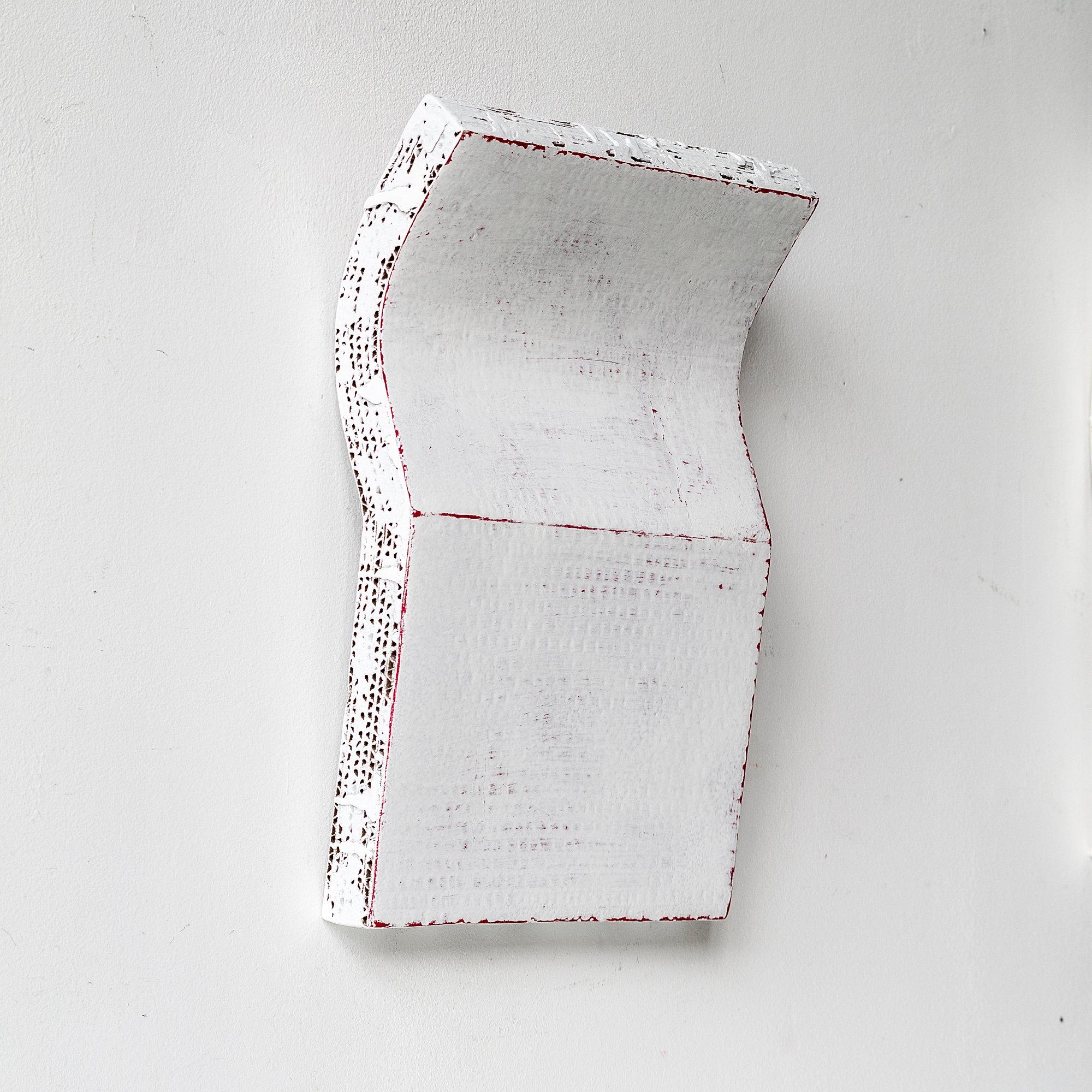 Abstract white textured sculpture with red edges mounted on a white wall.