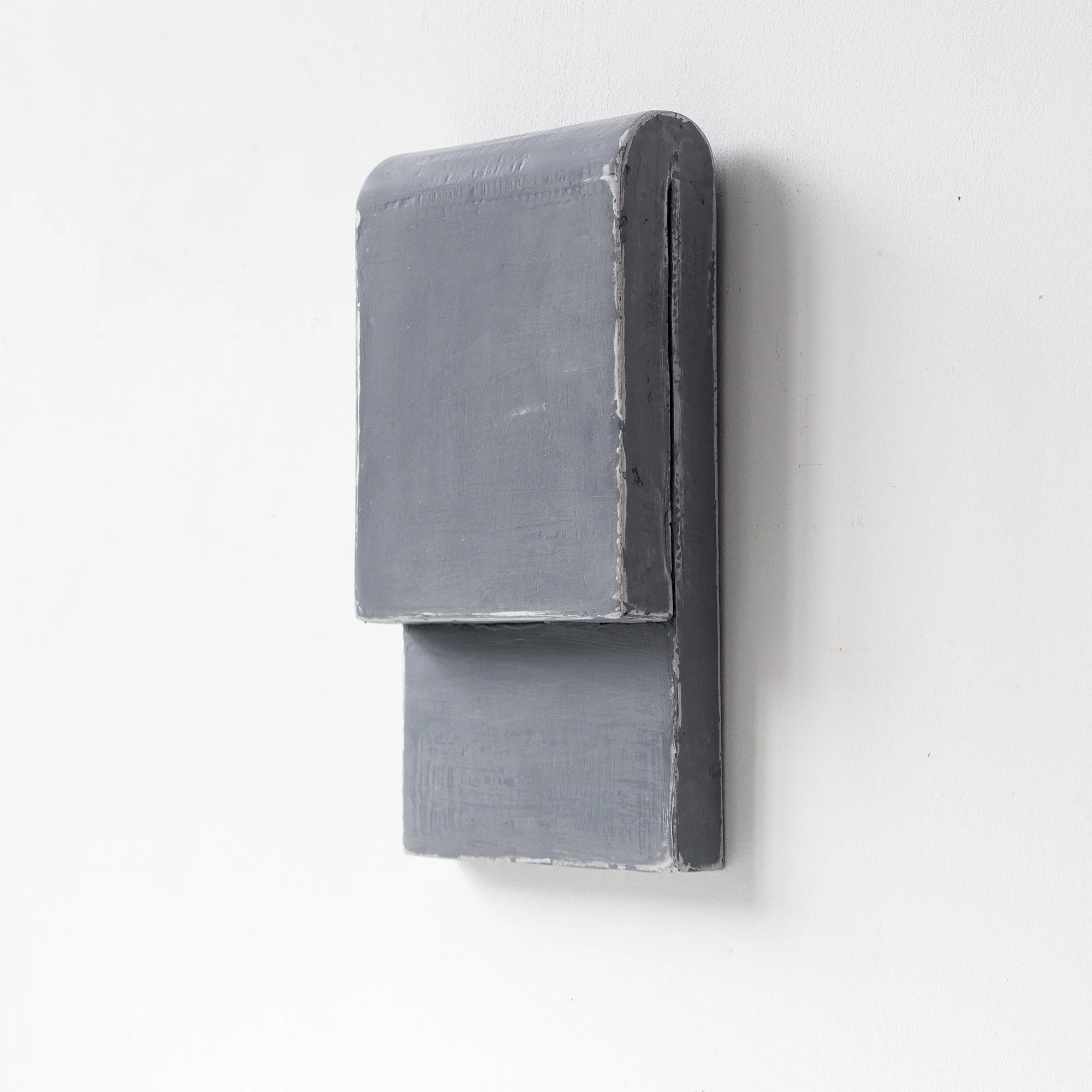 Gray minimalist wall-mounted sculpture with geometric shape against a white background.