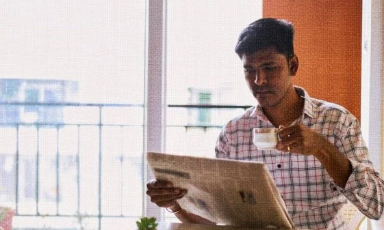 A young man reading a newspaper while having tea