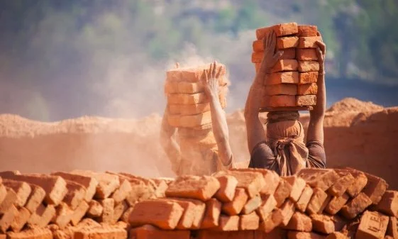 Two labourers at a construction site carrying bricks on their heads.