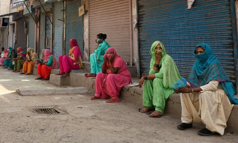 Women sitting outside shops with shutters down.