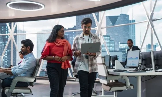 Two young professionals in an office overlooking high buildings.