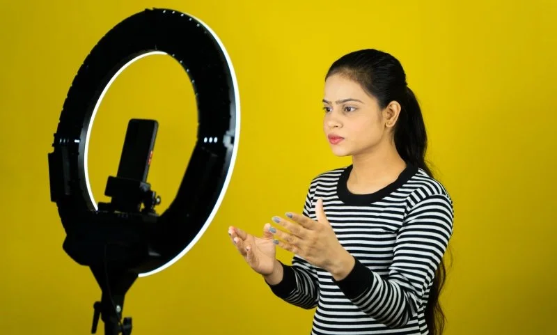 A young woman speaking to a phone camera with a ring light.