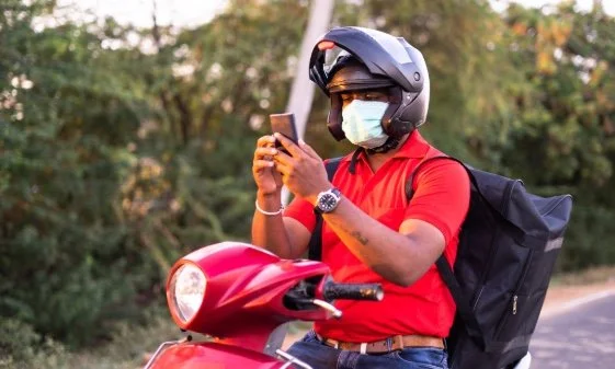 A delivery agent, sitting on his scooter, looking at his phone.