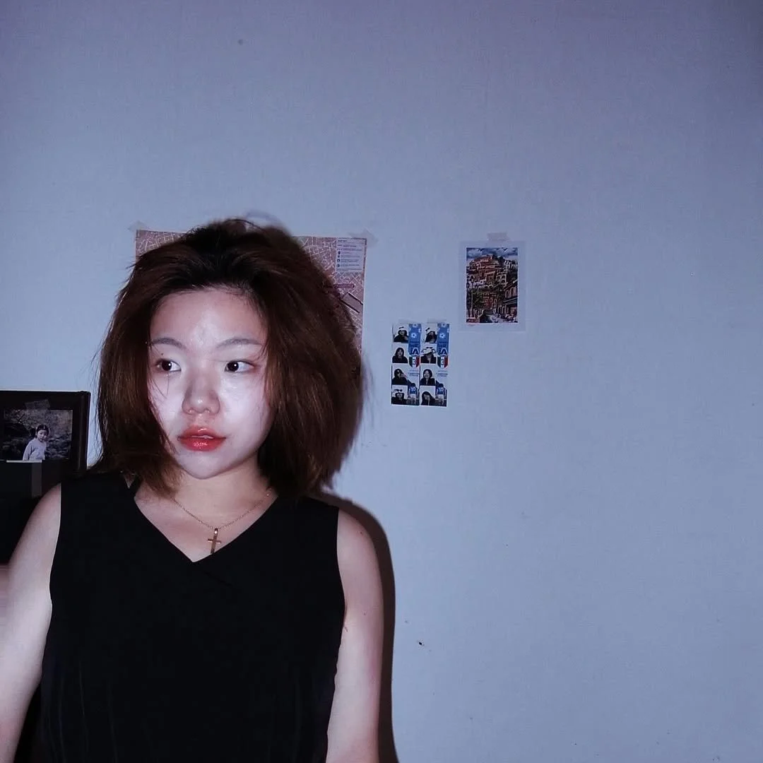 Woman in black outfit standing against a white wall with posters.