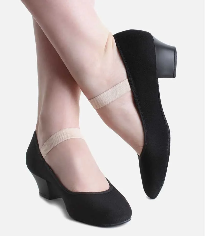 A person's feet wearing black low-heeled shoes with beige elastic straps around the ankles, against a plain background.