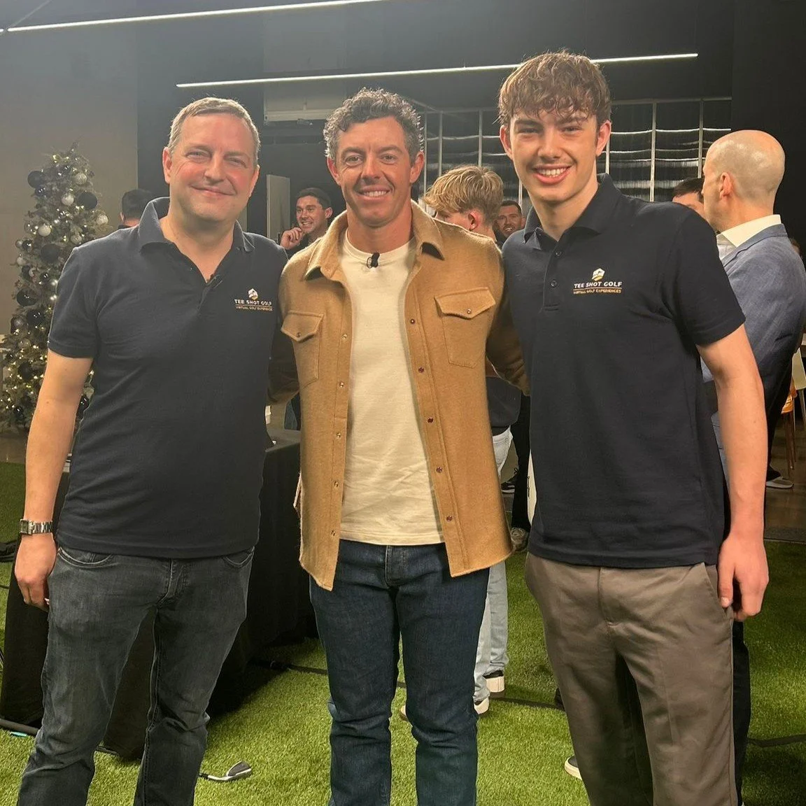 Three men standing together and smiling for the camera at an indoor event, with a Christmas tree in the background.