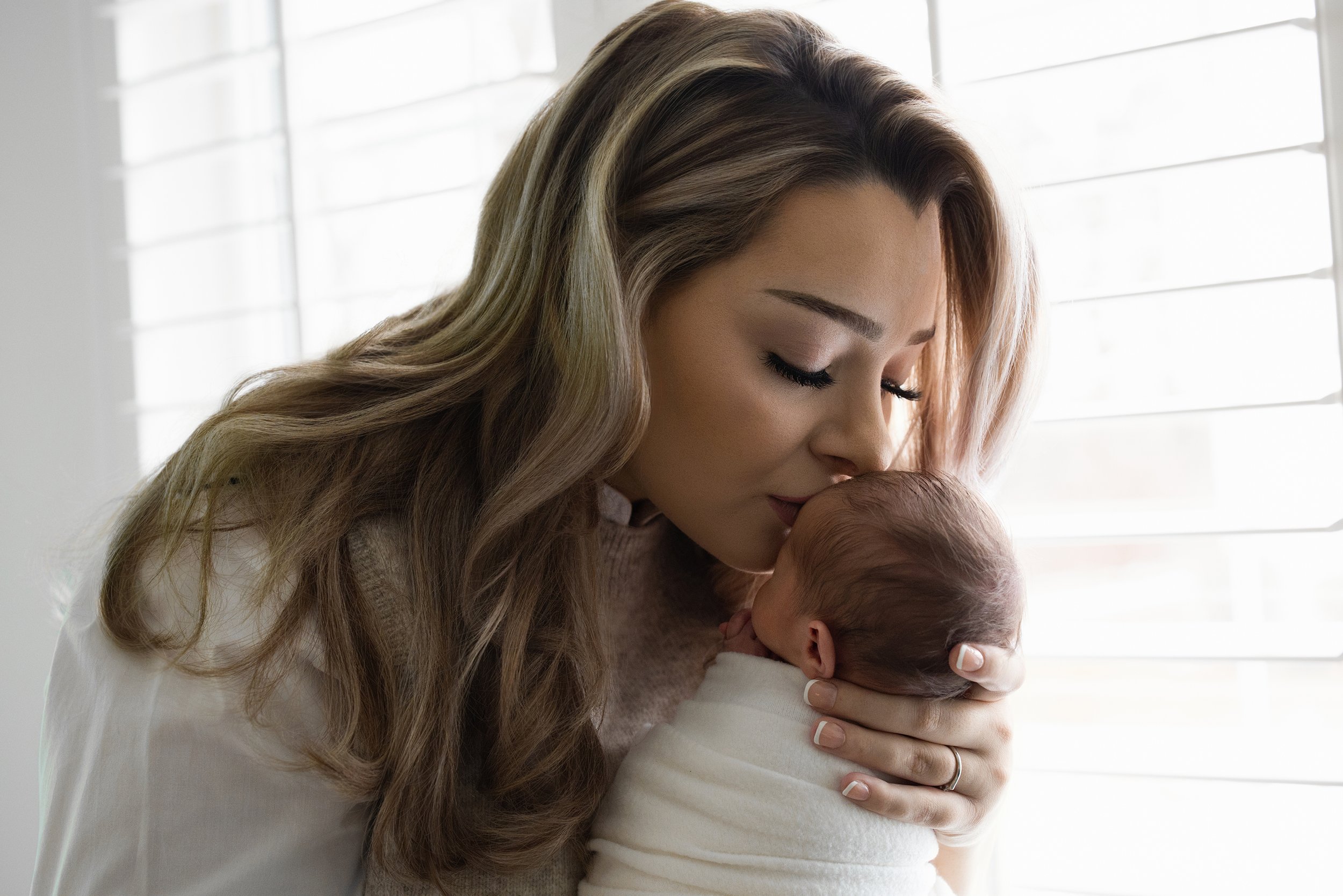 Mother kissing her newborn baby during a natural light in-home newborn photography session in Rochester Hills.