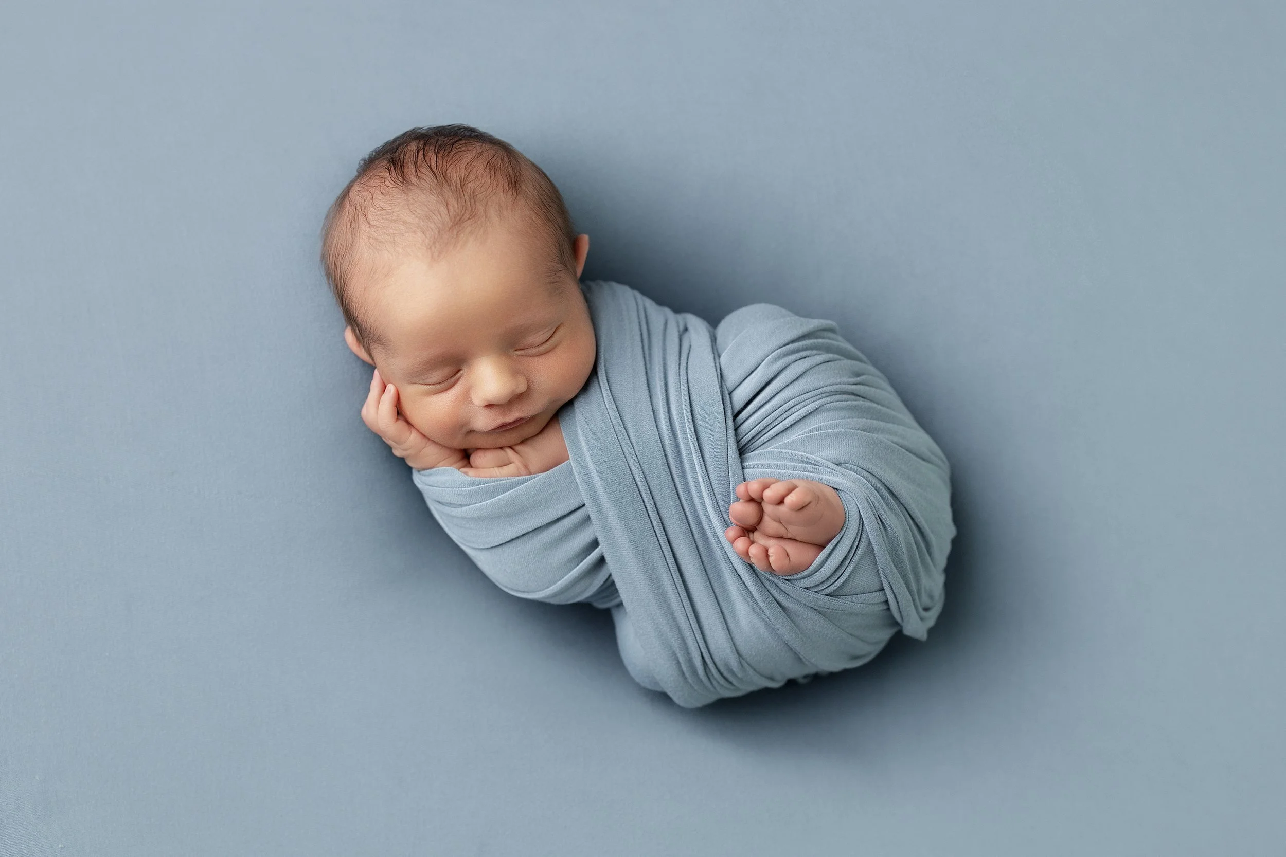 Newborn baby wrapped in a soft blue swaddle during a studio newborn photography session in Rochester Hills, Michigan.