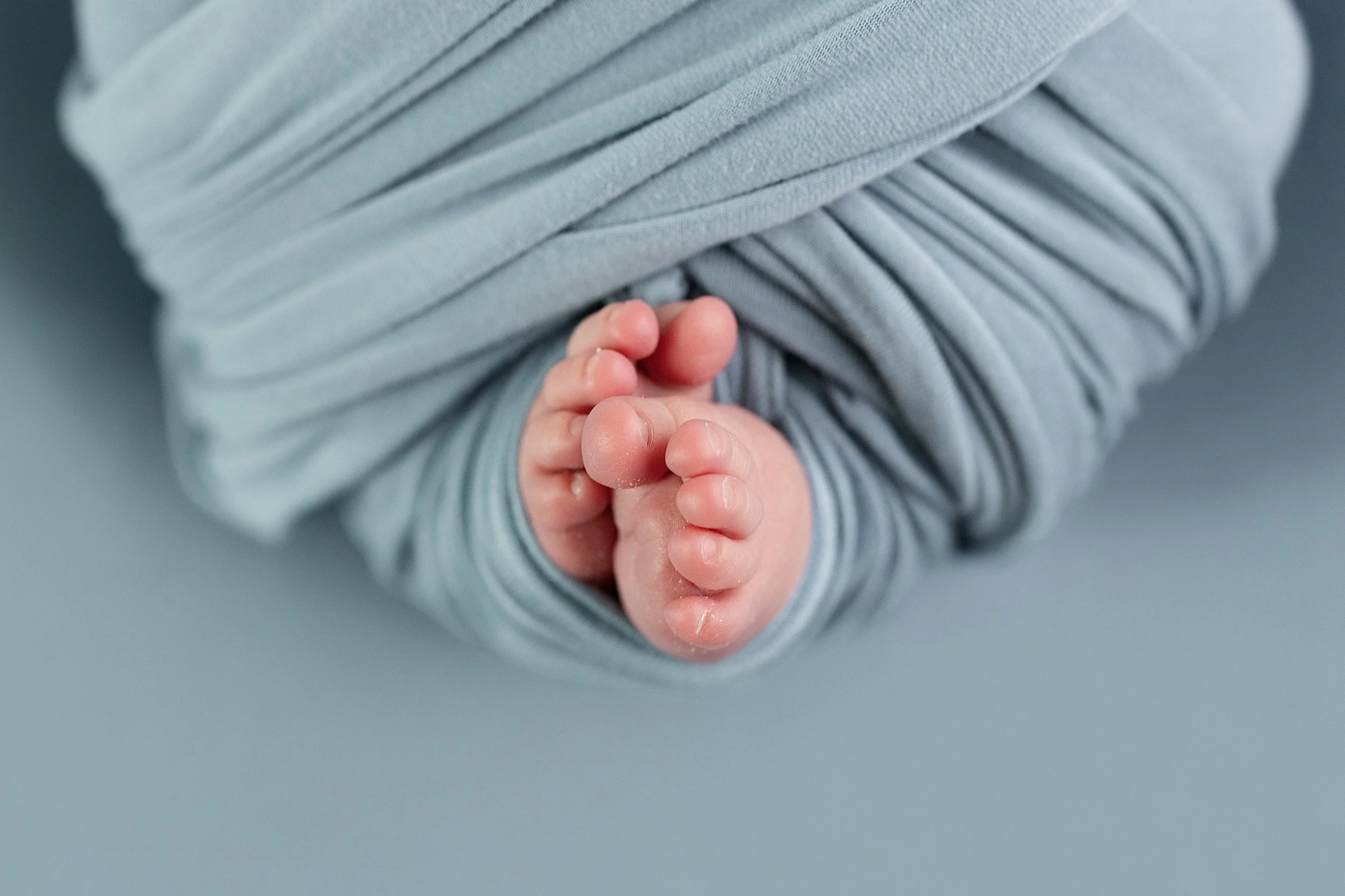 Close-up of newborn baby feet wrapped in a soft blue swaddle photographed by a Rochester Hills newborn photographer.