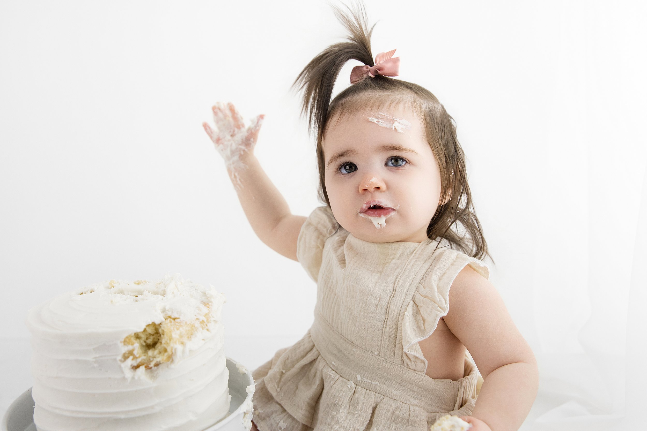 One year old baby girl enjoying cake smash during milestone photography session at Rochester Hills Michigan studio