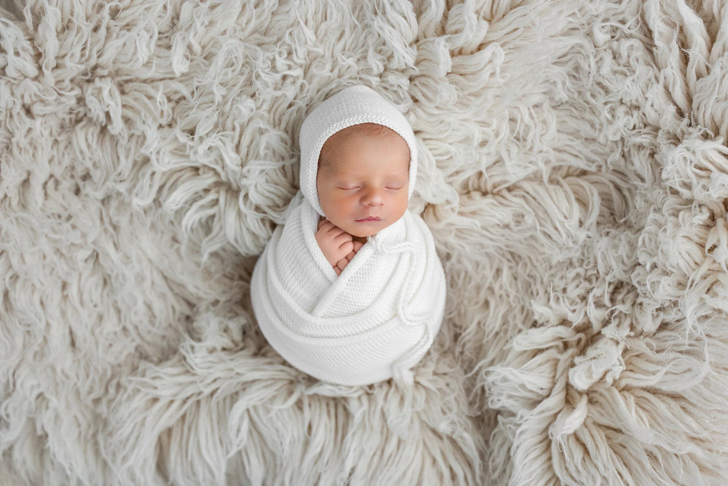 Wrapped newborn baby posed on a neutral textured blanket during a studio newborn photography session in Rochester Hills.