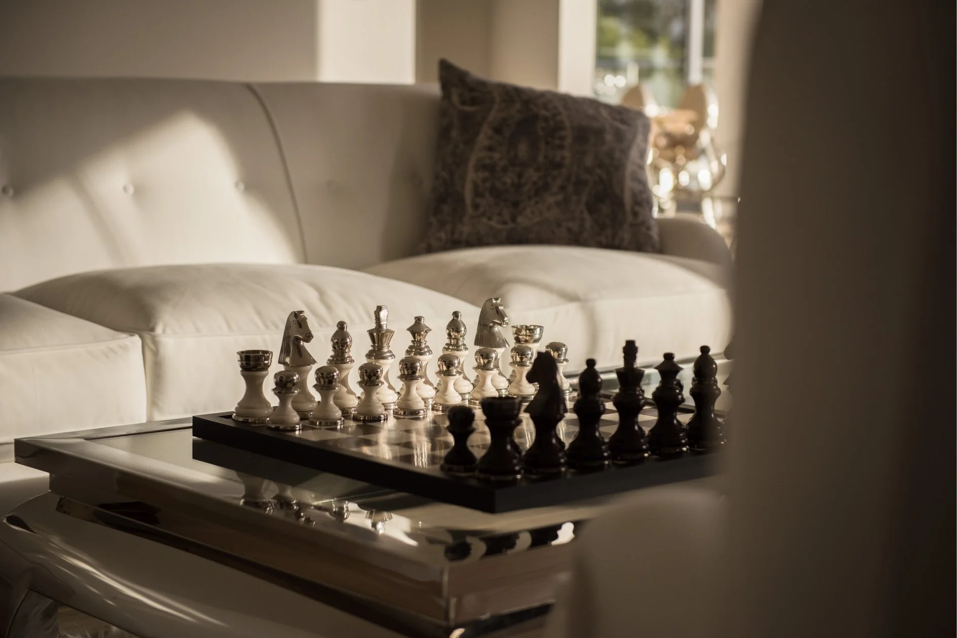 a substantial chess set sits on a chrome coffee table with a white sofa behind