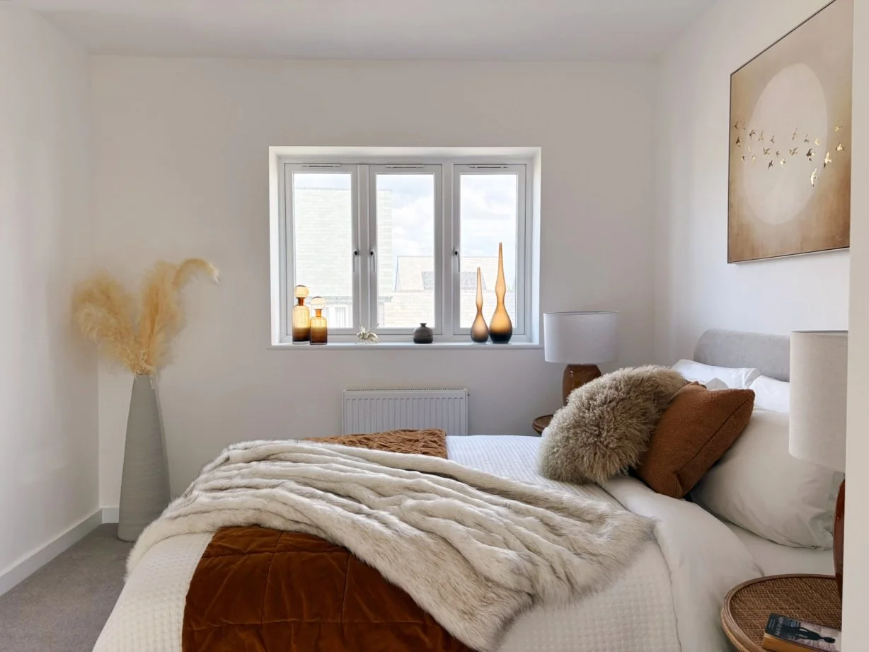 A bedroom for a modern house in neutral and brown tones from white through beige, russet and burnt orange.  A fur throw, fluffy cushions and pampas stems add texture and warmth